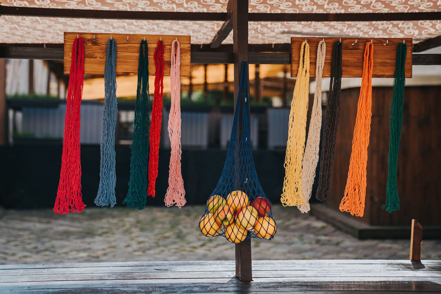 Colorful macrame mesh shopping bags hanging outdoors, with one bag filled with fresh oranges.
