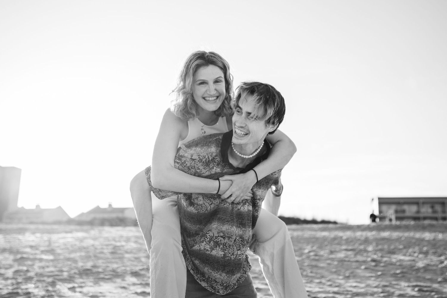 Black and white photos of a playful couple running and embracing on a sandy beach.