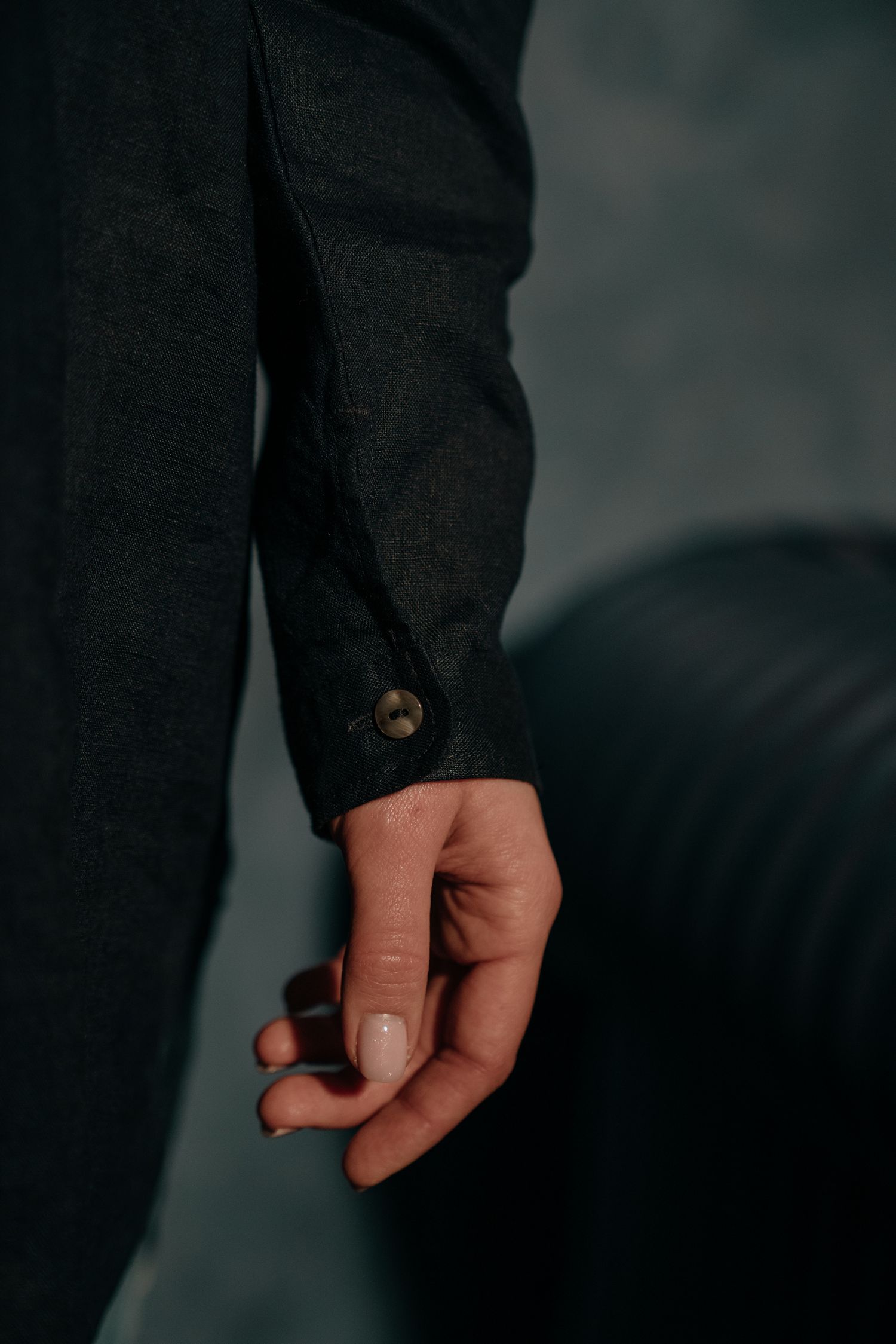 Close-up of a hand with manicured nails wearing a dark charcoal button-cuff jacket sleeve.