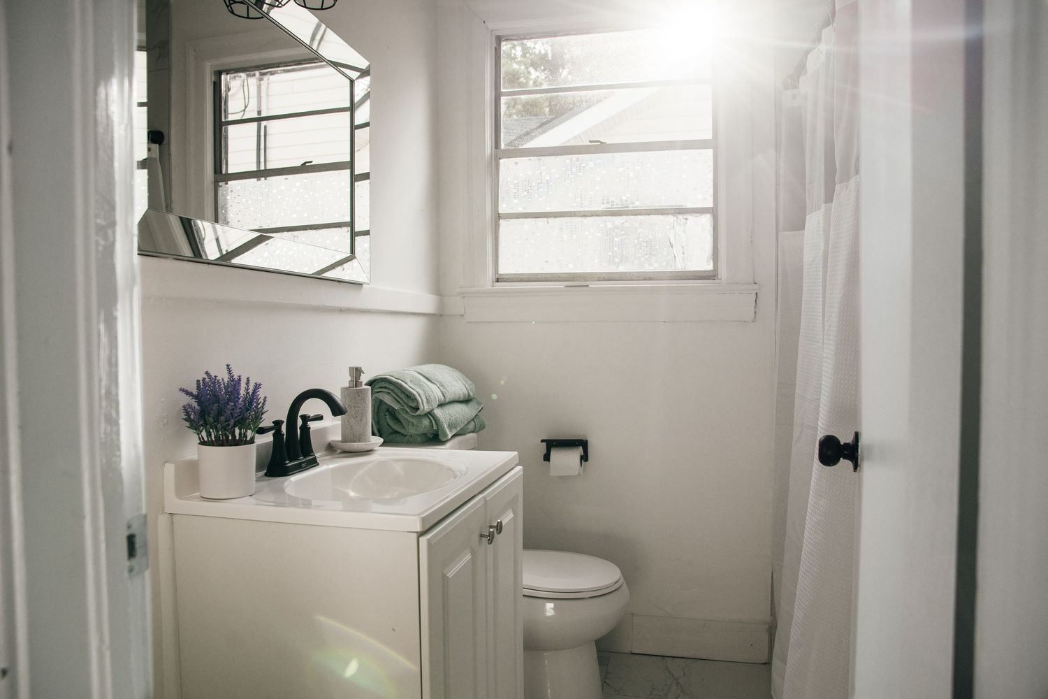 Bright white bathroom with vanity, mirror, toilet, and shower curtain in a clean, minimalist design.