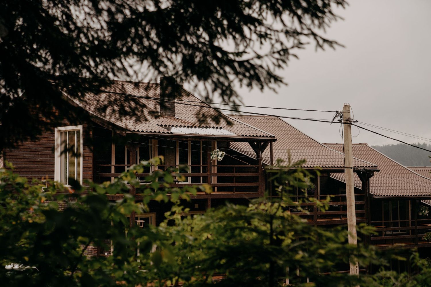 Rustic wooden cabin with covered porch surrounded by lush green trees and mountains in the background.