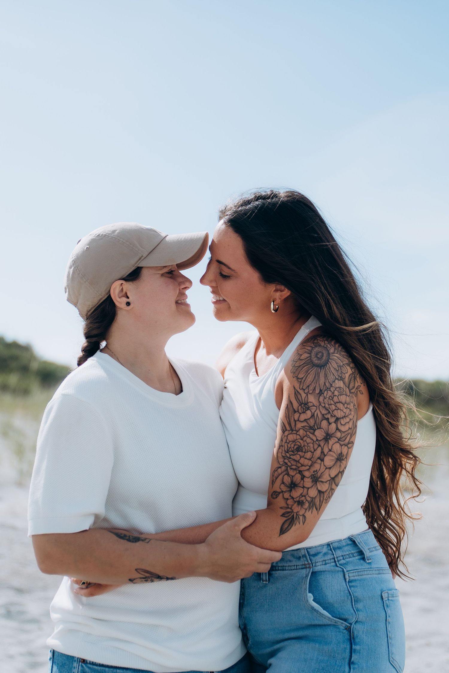 Couple in white shirts and denim sharing affectionate moment on beach.