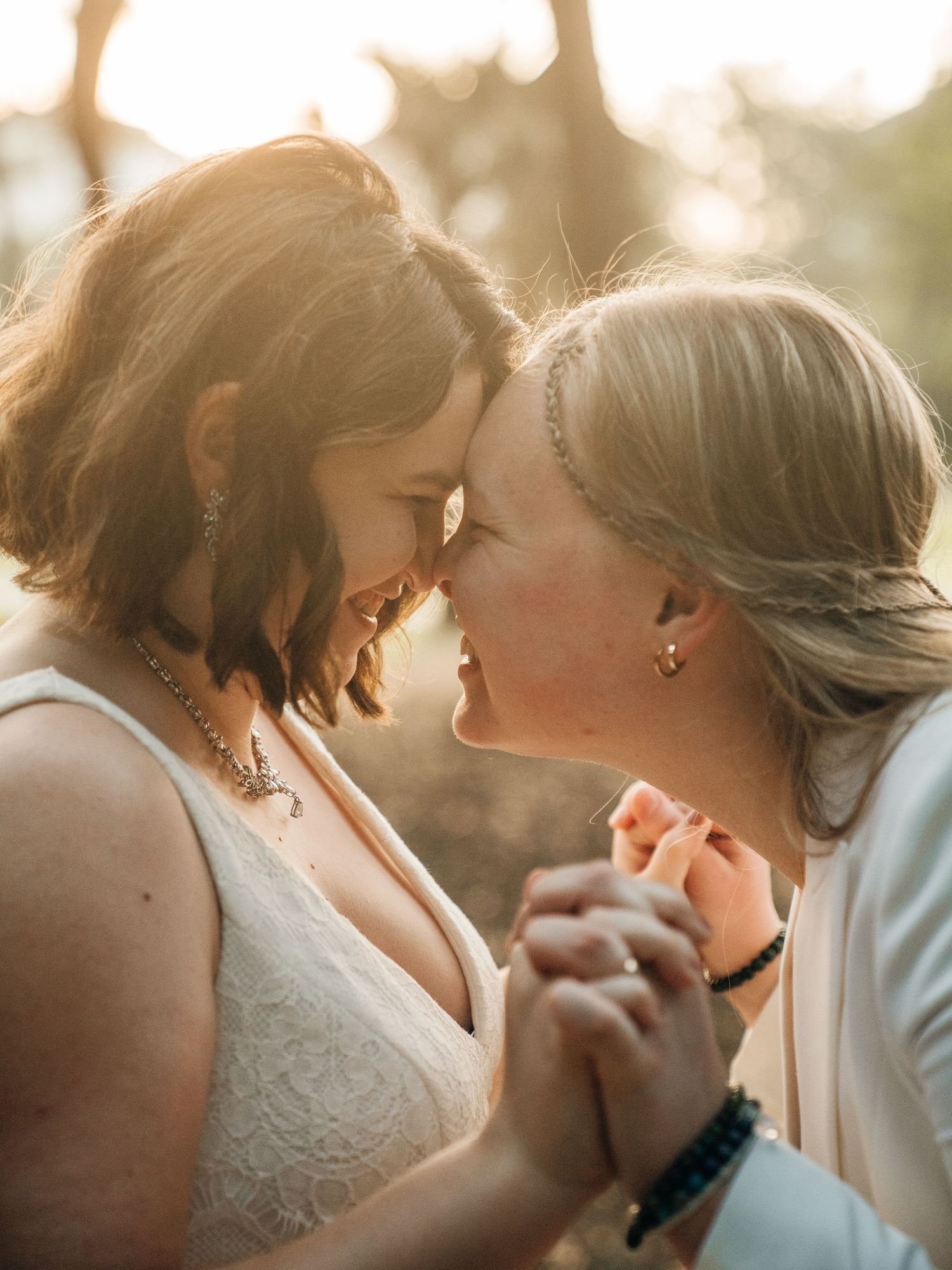 An intimate moment shared between two people in white wedding attire during a sunset photoshoot.