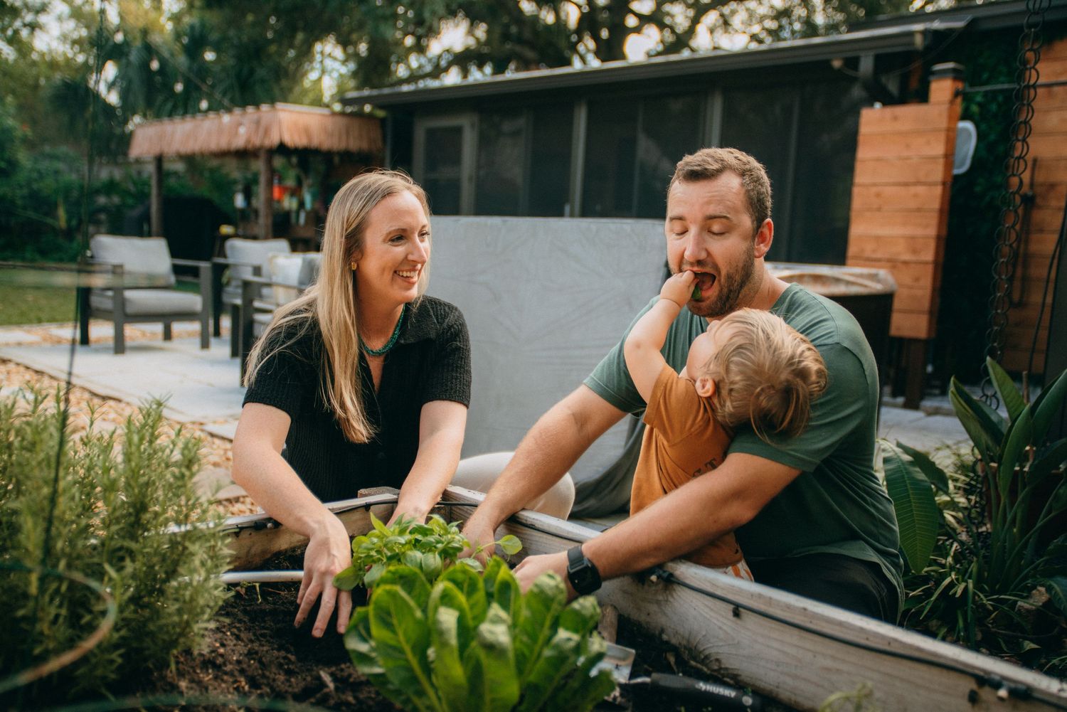 A playful outdoor family moment captured in a garden setting with natural greenery in the background.
