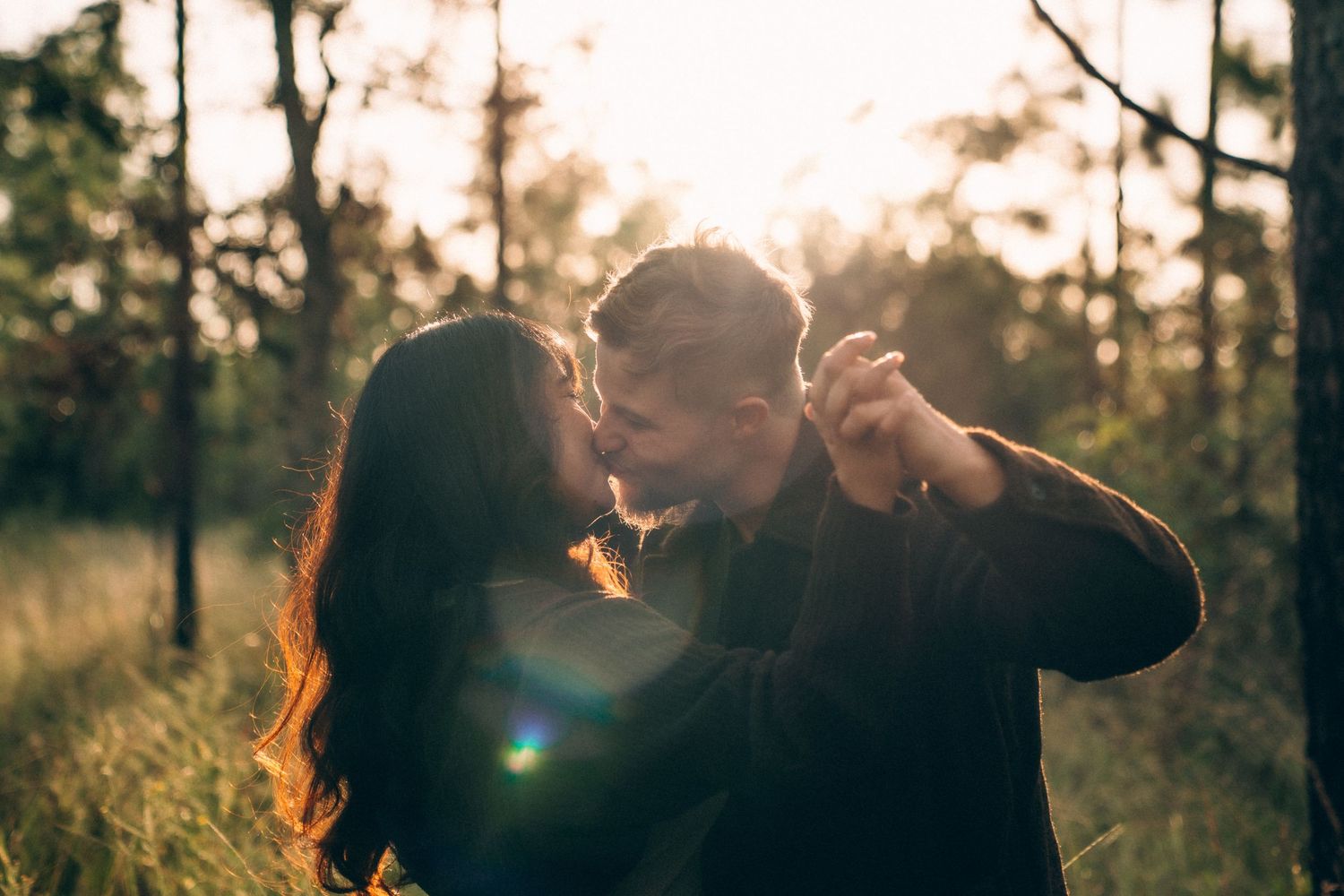 Couple shares intimate moment in golden sunlight with trees silhouetted in background.
