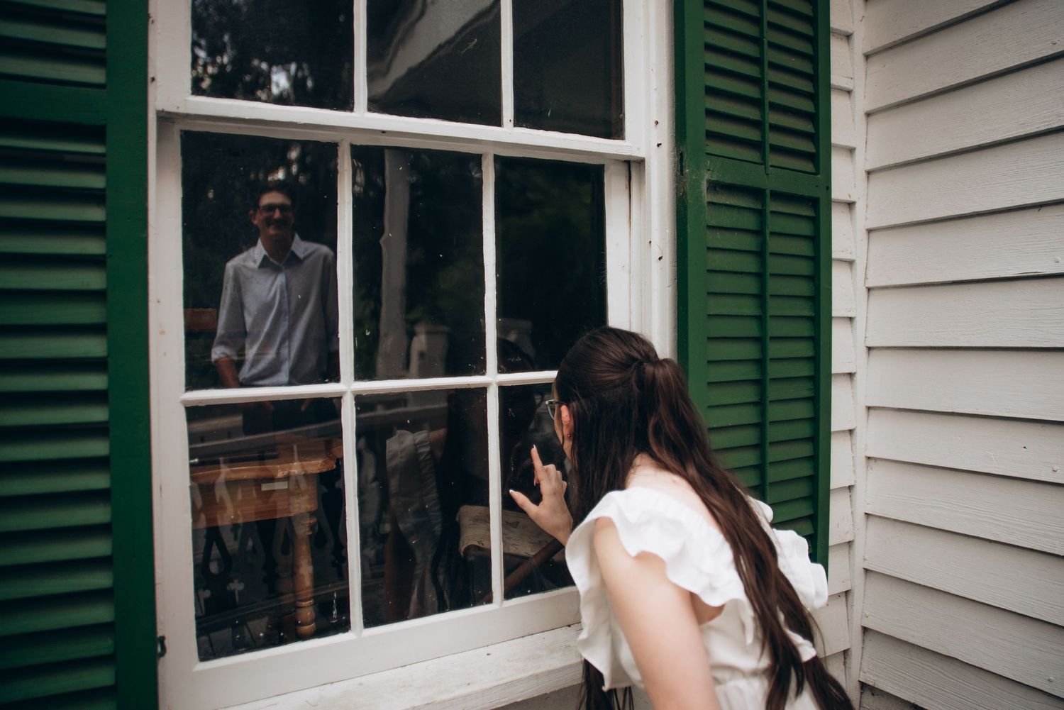Historic white clapboard house with dark green shutters and large windows in natural lighting.
