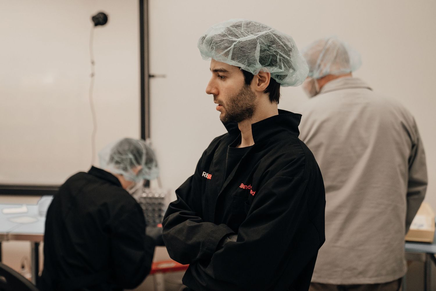 Food workers in hairnets and black uniforms standing in a commercial kitchen food production facility.