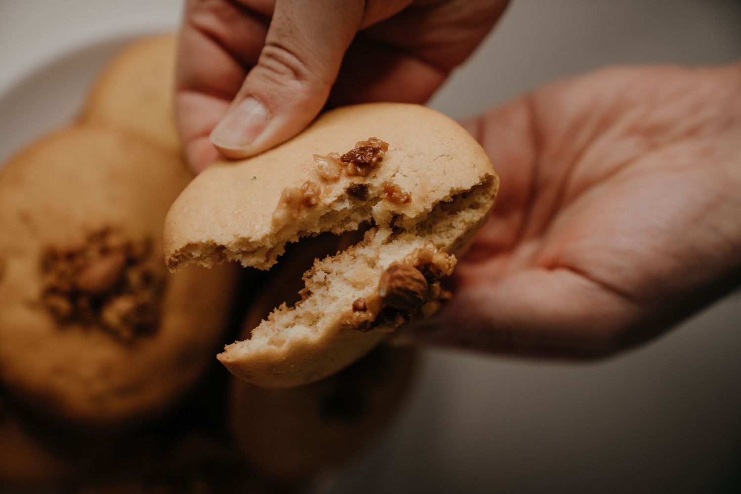 Hands breaking open a soft cookie filled with crumbled walnut filling on a white plate.