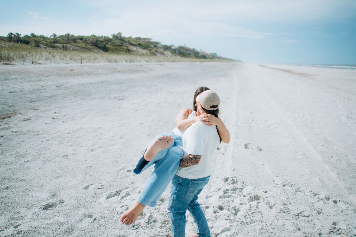 Playful couple running and dancing on empty beach under blue sky.