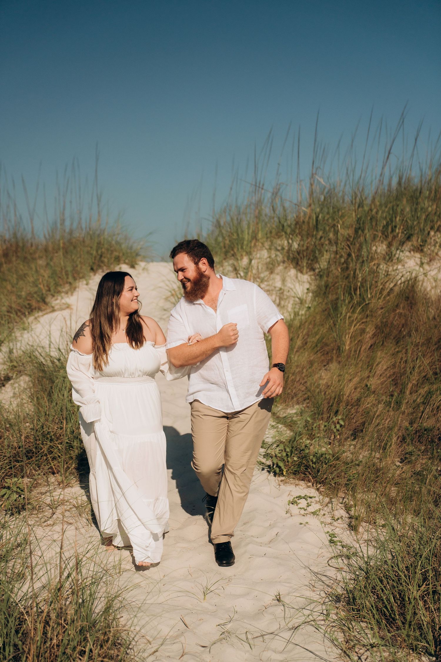 Happy couple walking and laughing together on sandy beach path.