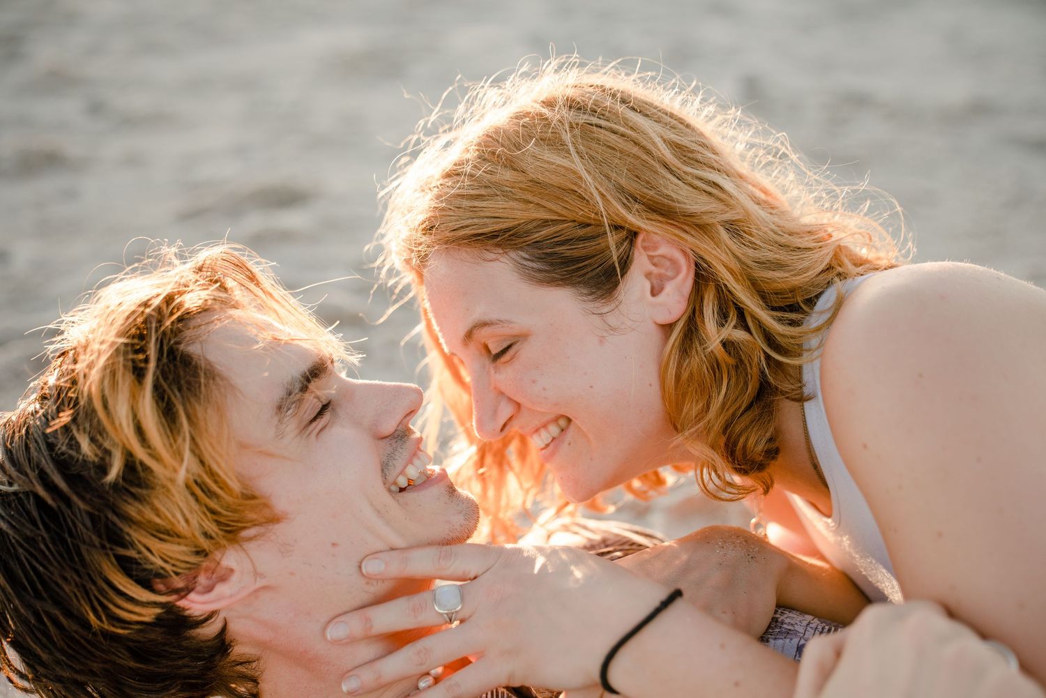 Intimate couple embracing on beach at golden hour with sunlight streaming through their hair.