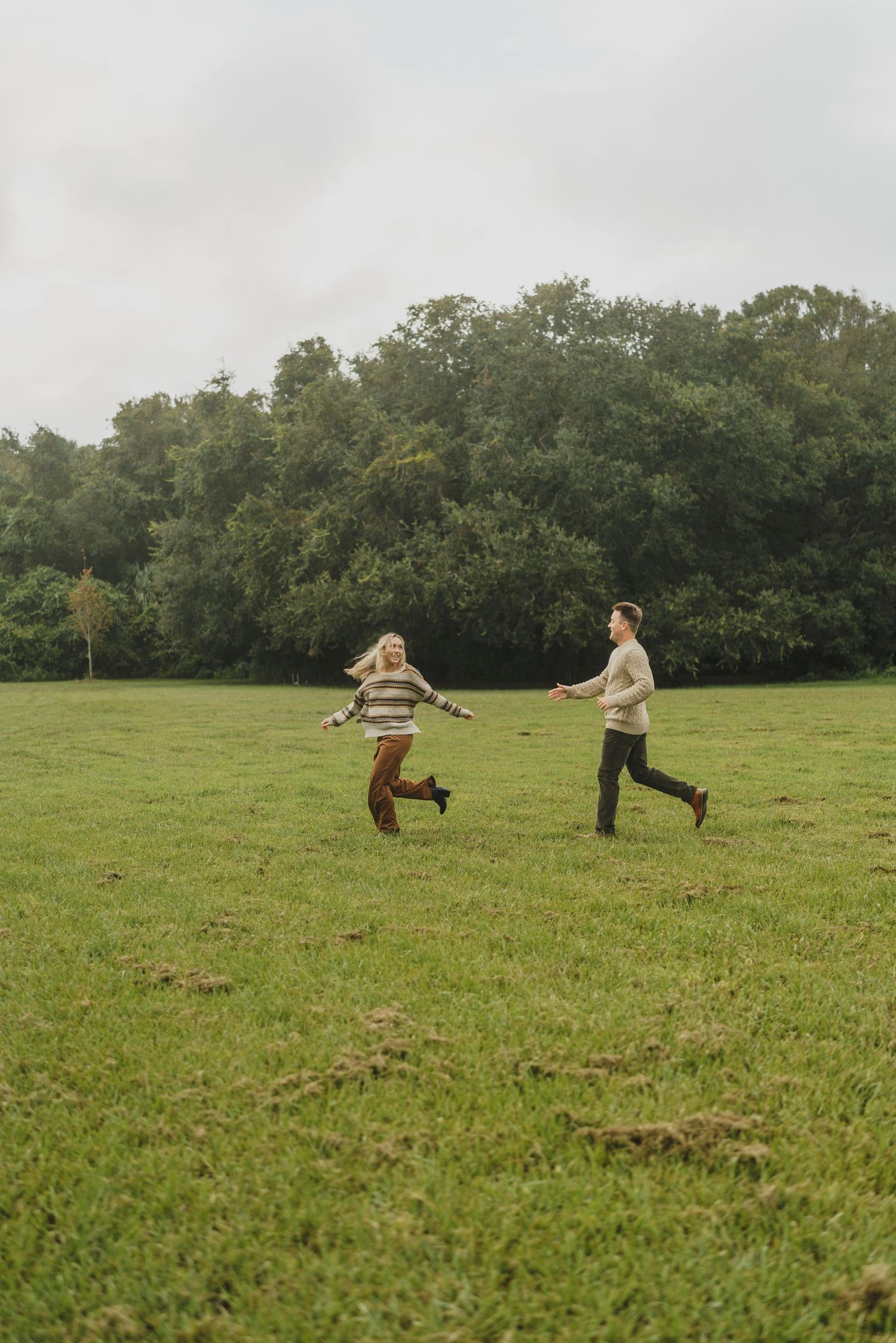 People playing and running together in a spacious green field surrounded by trees.