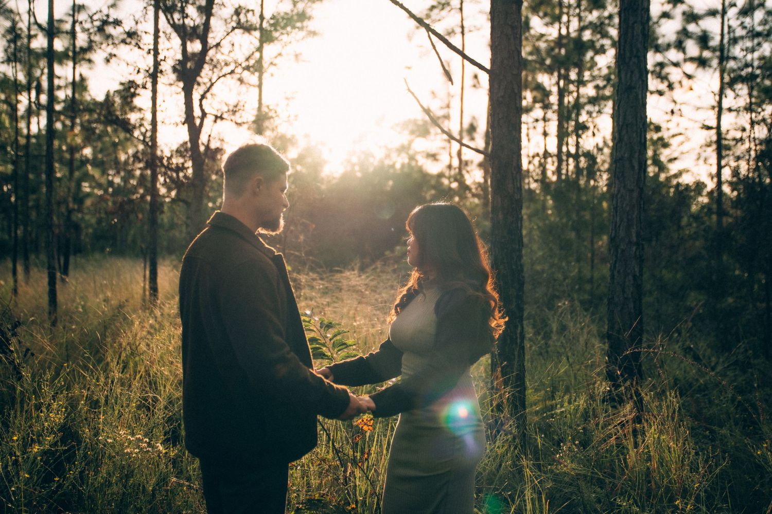 Silhouetted couple embraces in golden sunlit forest during romantic outdoor photo session at sunset.
