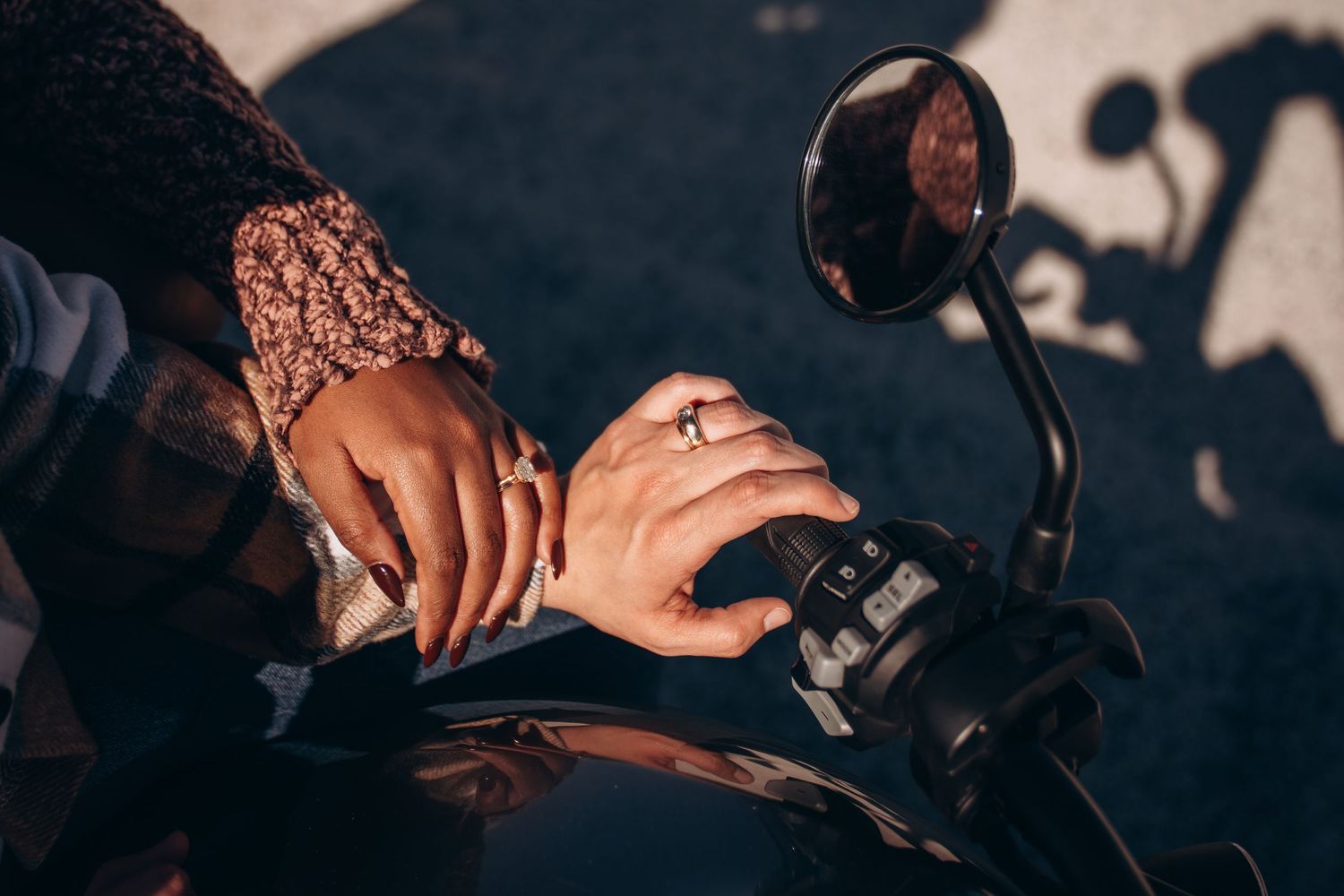 Close-up shot of hands with an engagement ring resting on a motorcycle handlebar.