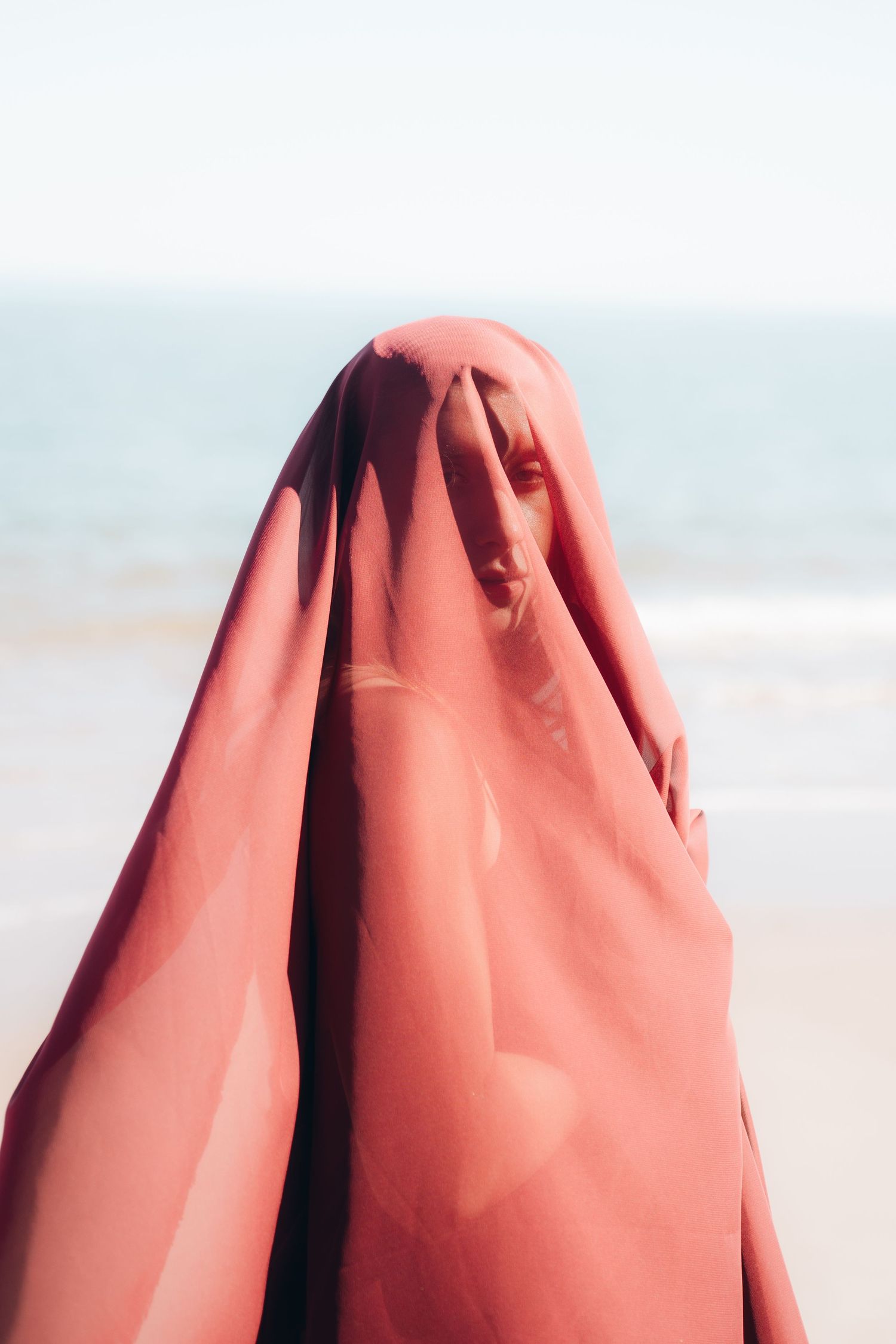 Close-up view of coral-colored fabric creating soft folds and ripples against a bright background.