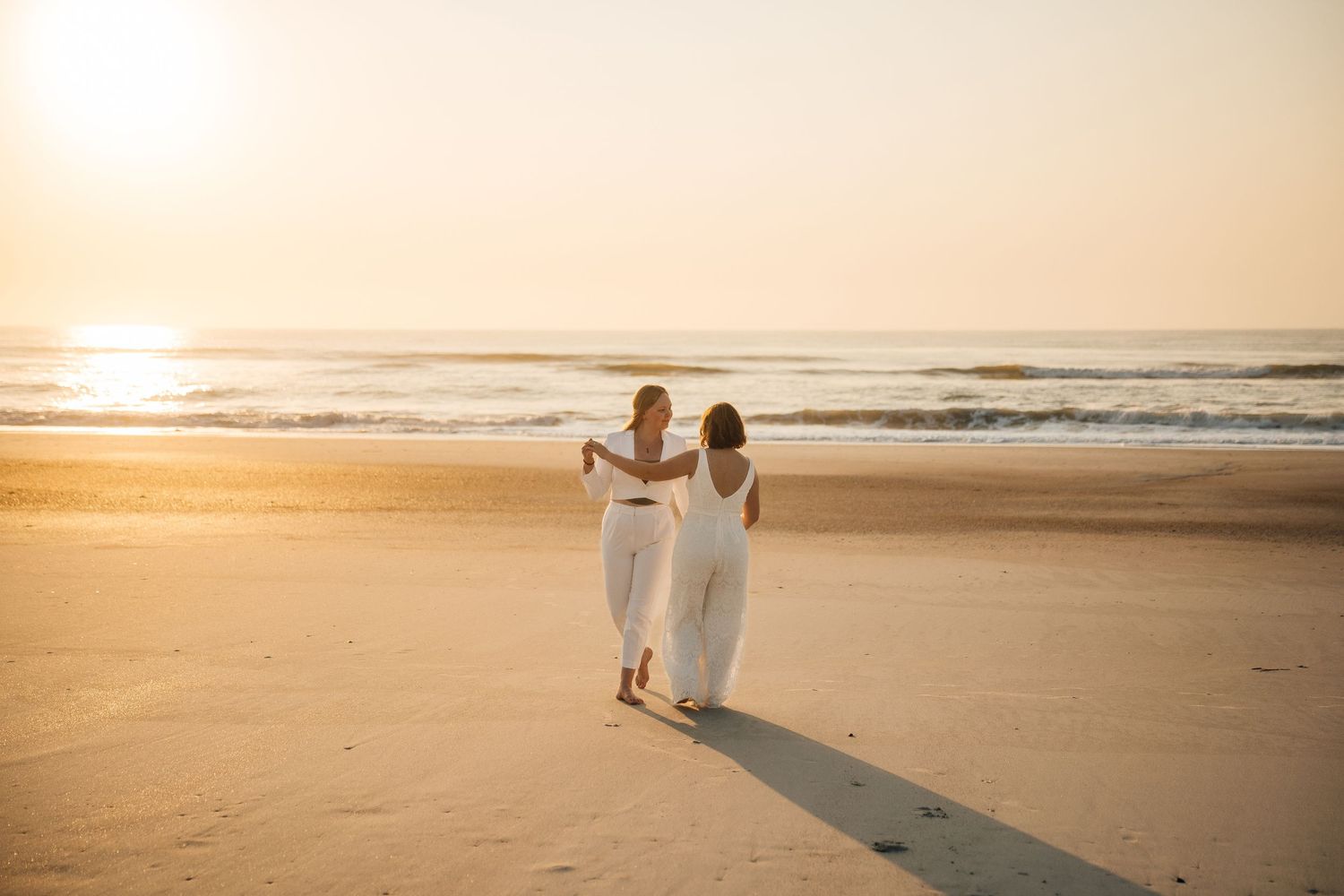 A wide panoramic beach scene at sunset with distant figures near the ocean.
