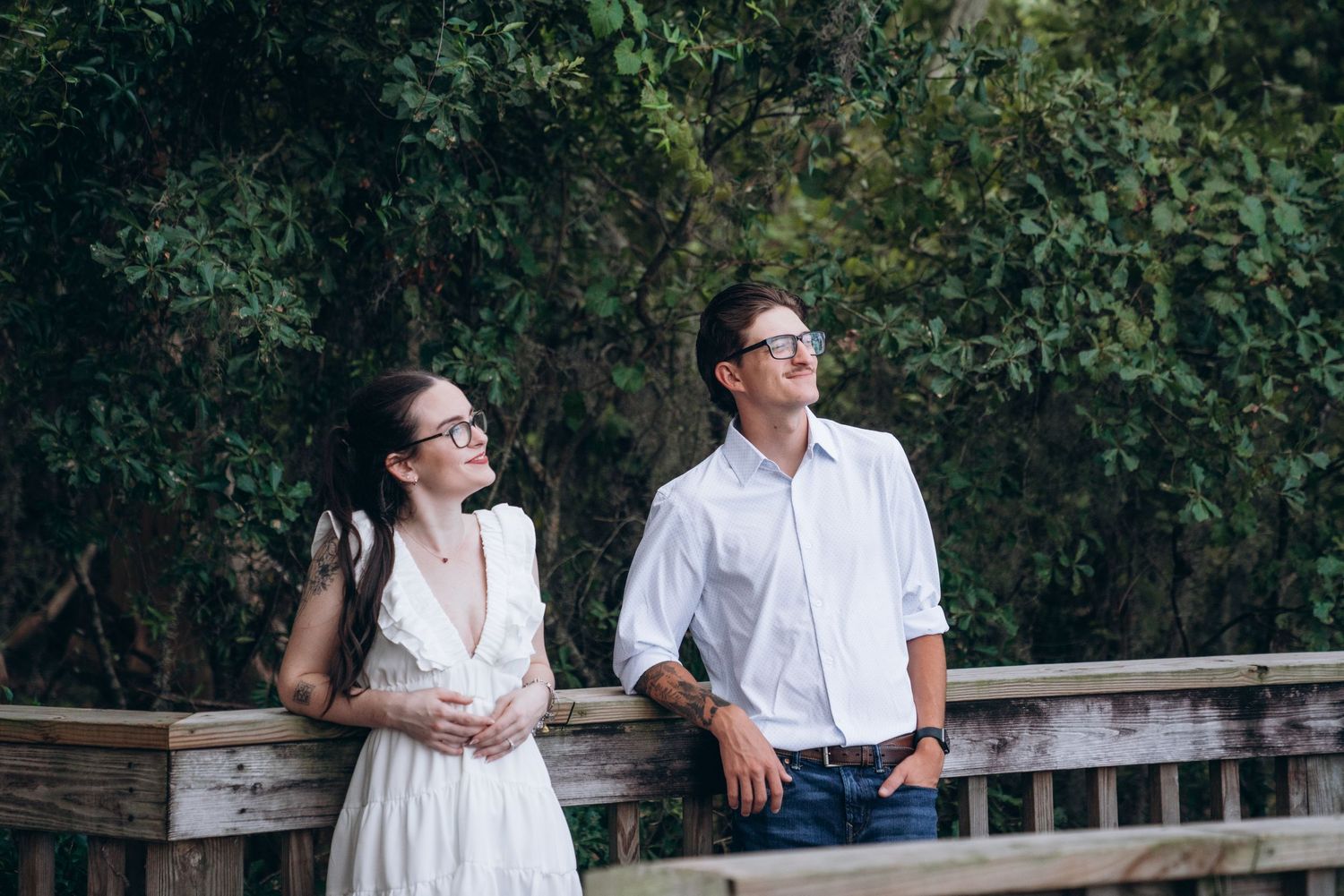 A romantic couple shares tender moments together while sitting on a wooden railing in a garden setting.