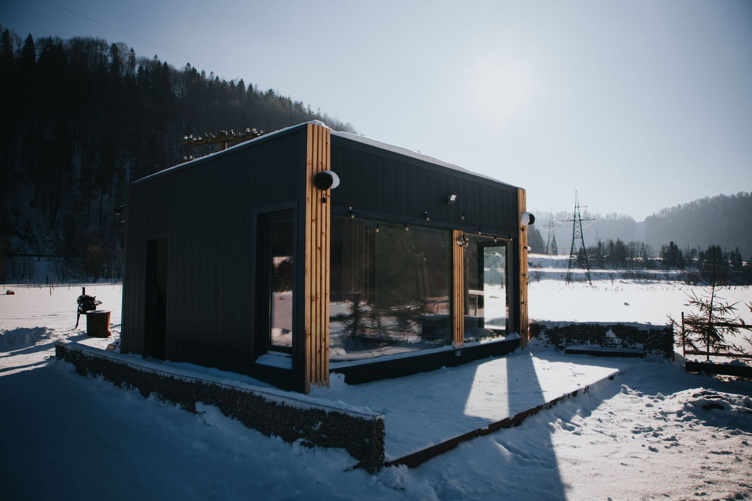 Modern black and wood tiny cabin in snowy mountain landscape on sunny winter day.