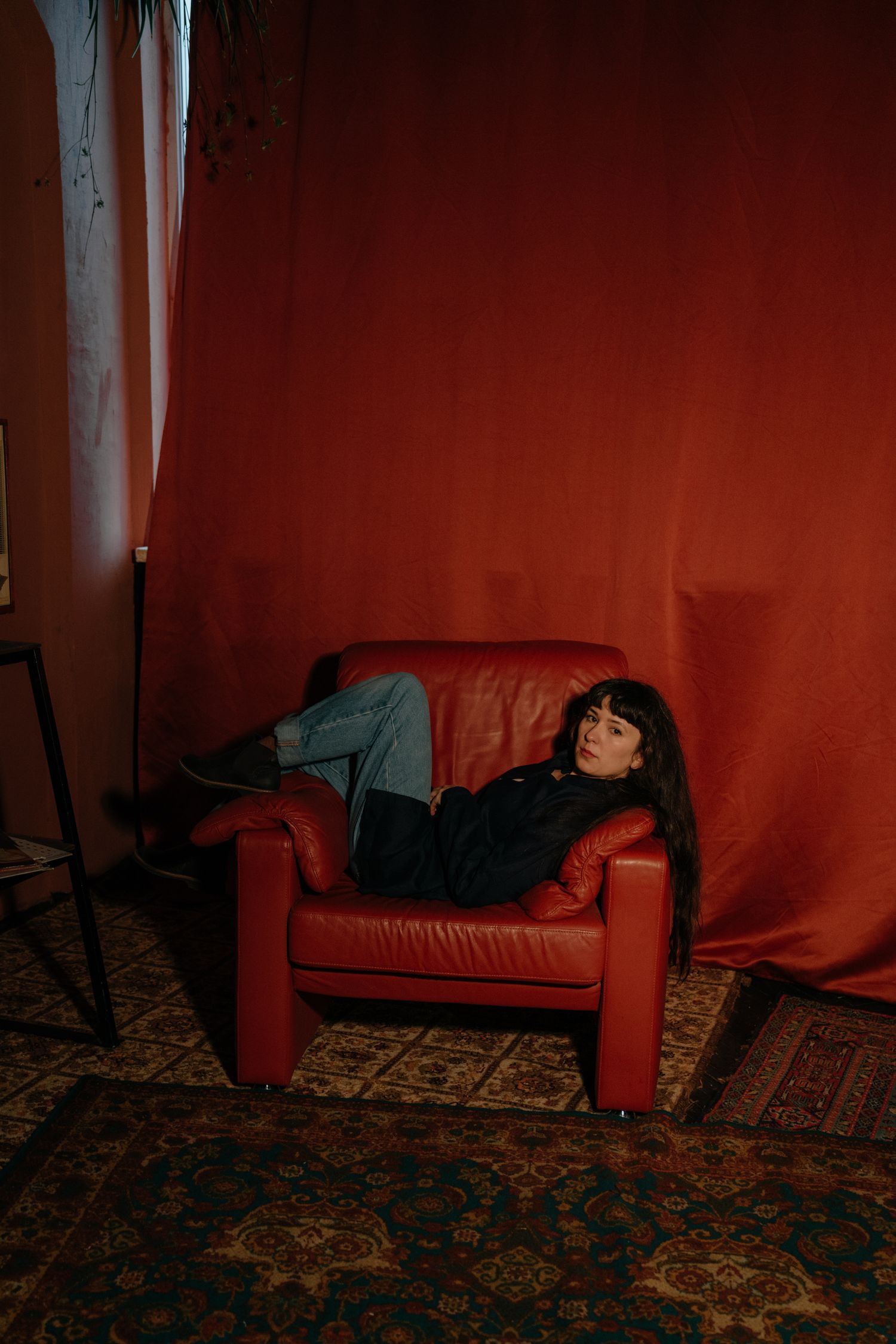 Person relaxing on a red leather armchair against a red draped background on a patterned rug.