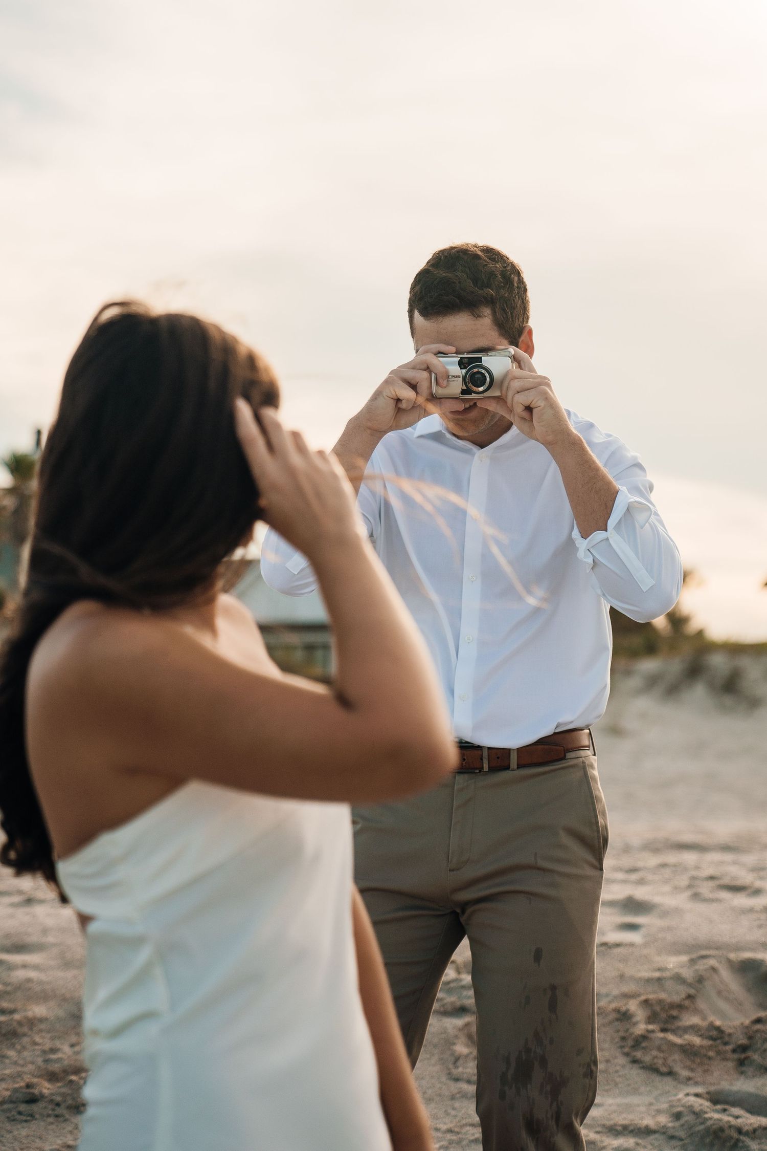 A couple taking photos of each other on a beach with cameras during golden hour.