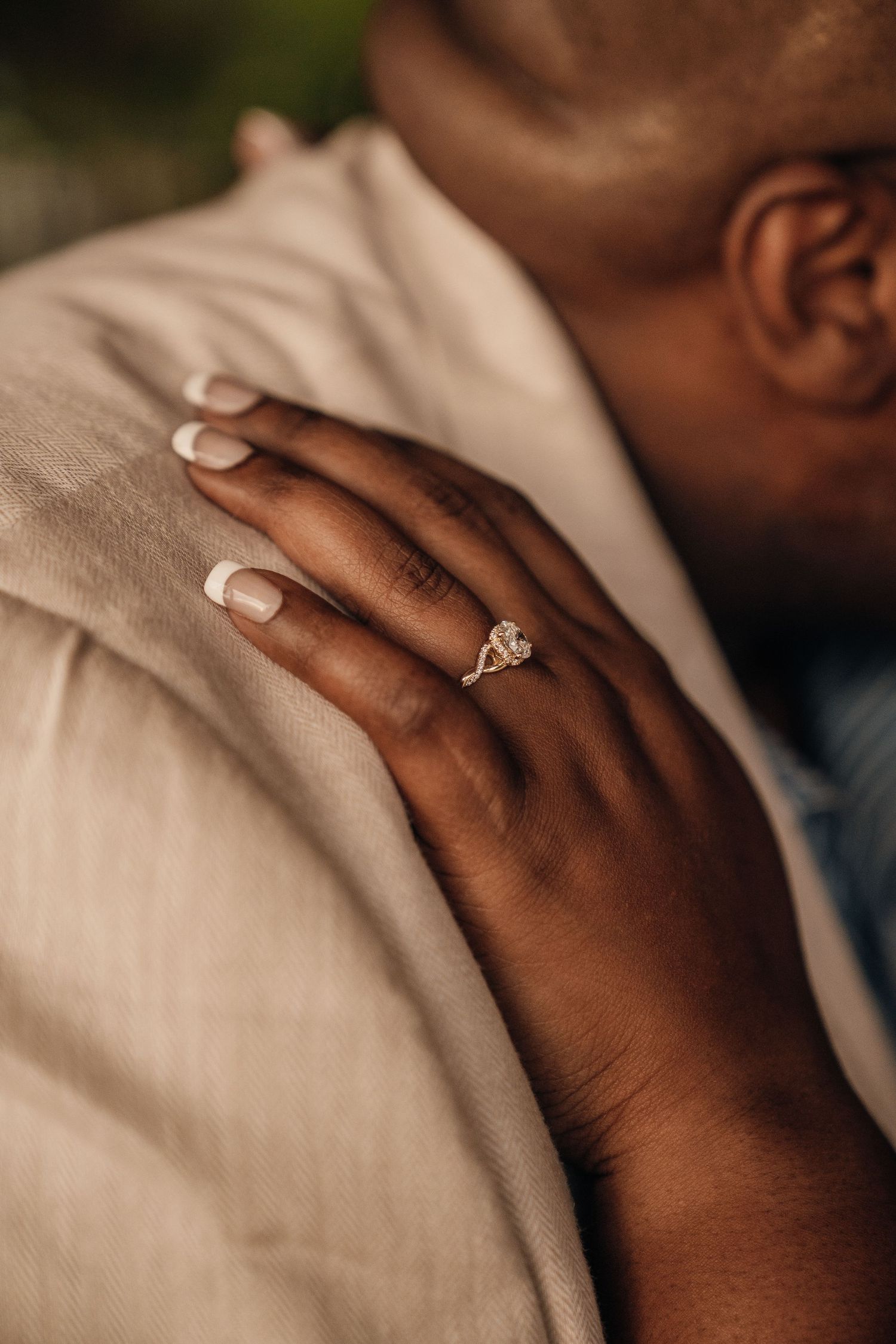 Close-up of an engagement ring on a hand resting against a cream-colored jacket.
