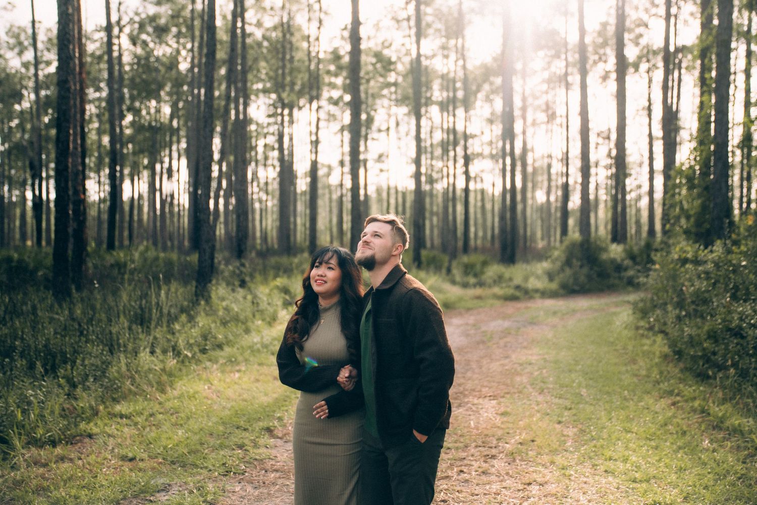 A couple walks hand in hand through a misty pine forest with sunlight filtering through the trees.
