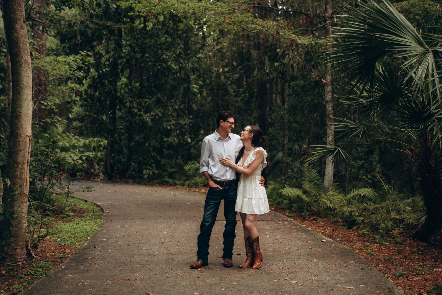A couple shares a romantic moment on a wooded boardwalk trail surrounded by palm trees and Spanish moss.