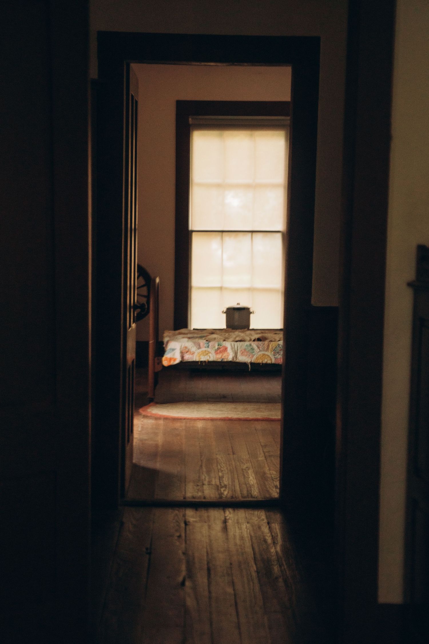 Dark interior hallway with wooden floors leading to a sunlit room.