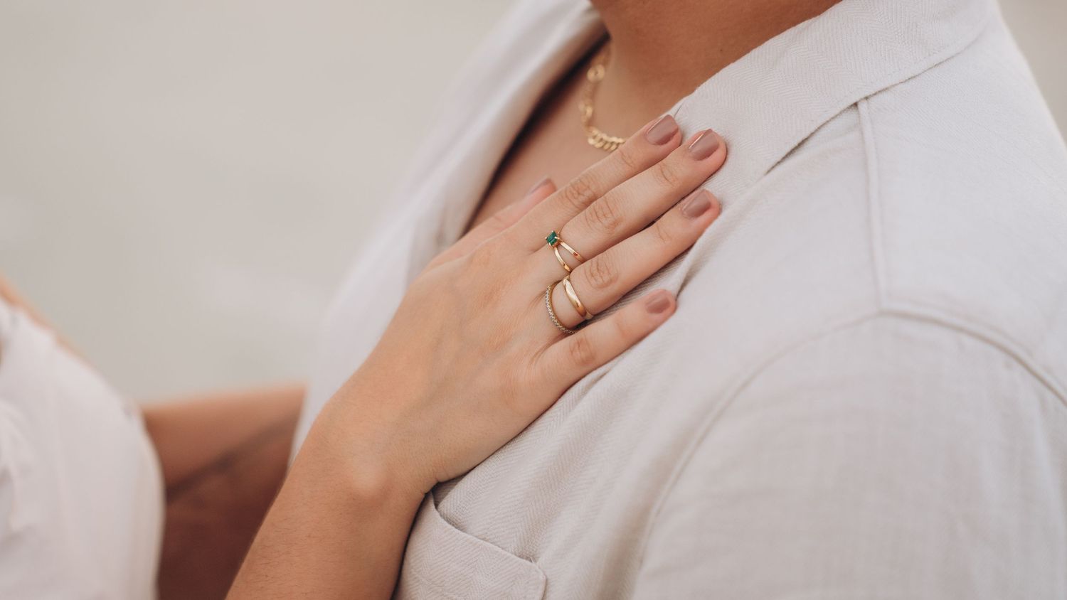 Detail shot of hands tenderly embracing in white clothing against a light background.
