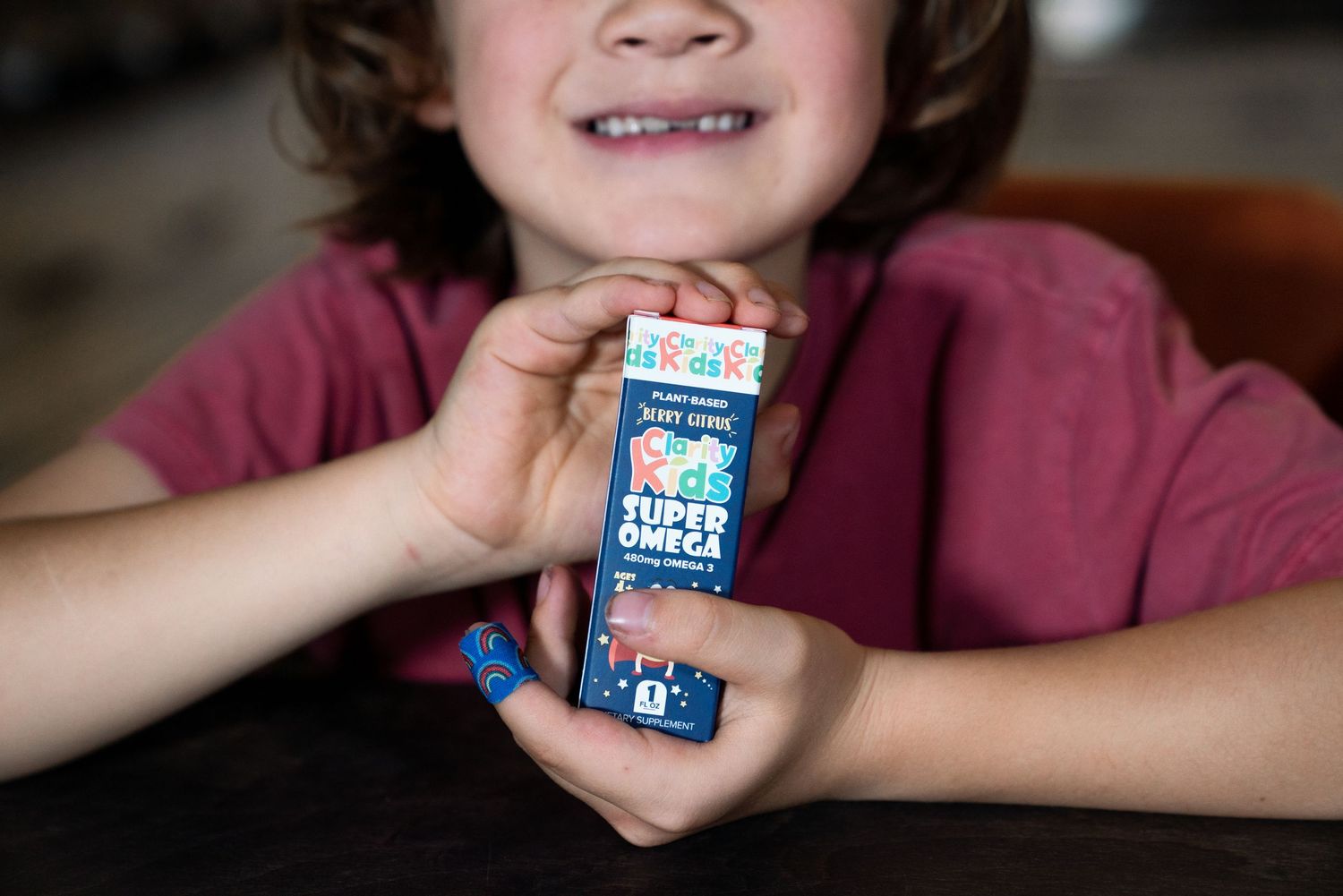 Child holding a small Super Omega supplement box, smiling with a missing tooth.