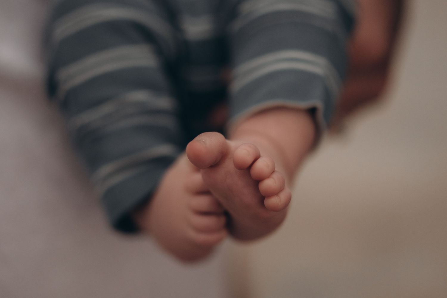 Close-up of tiny newborn baby feet wearing striped gray pants, soft focus background.