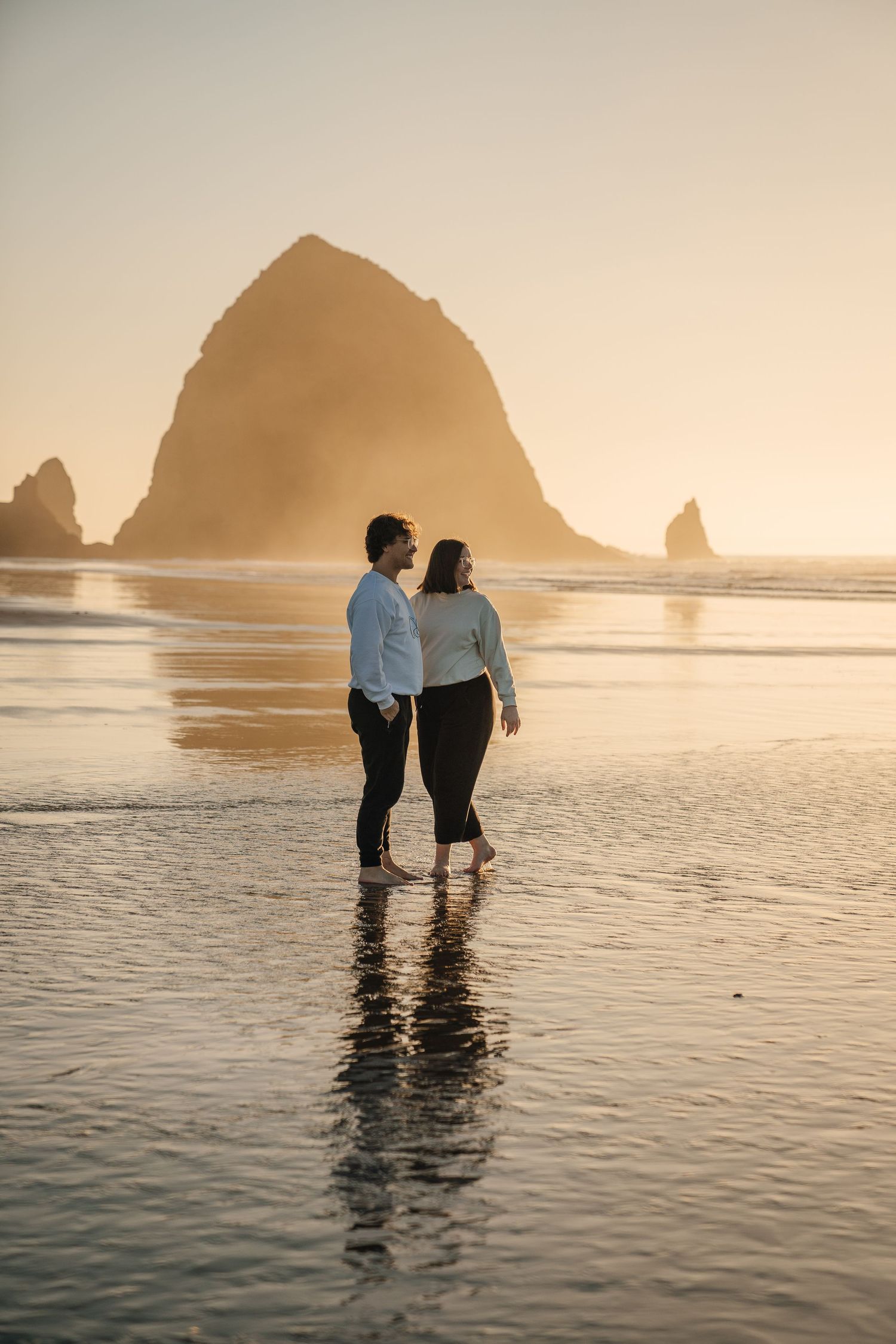 Two silhouettes standing in shallow ocean water with large rock formations in the background.