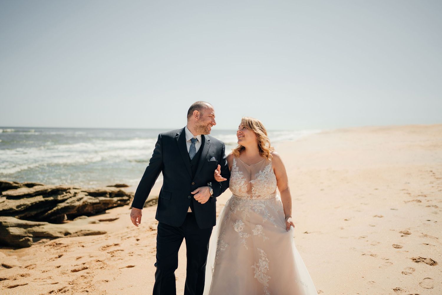 Romantic beach photoshoot with couple walking along sandy shoreline.