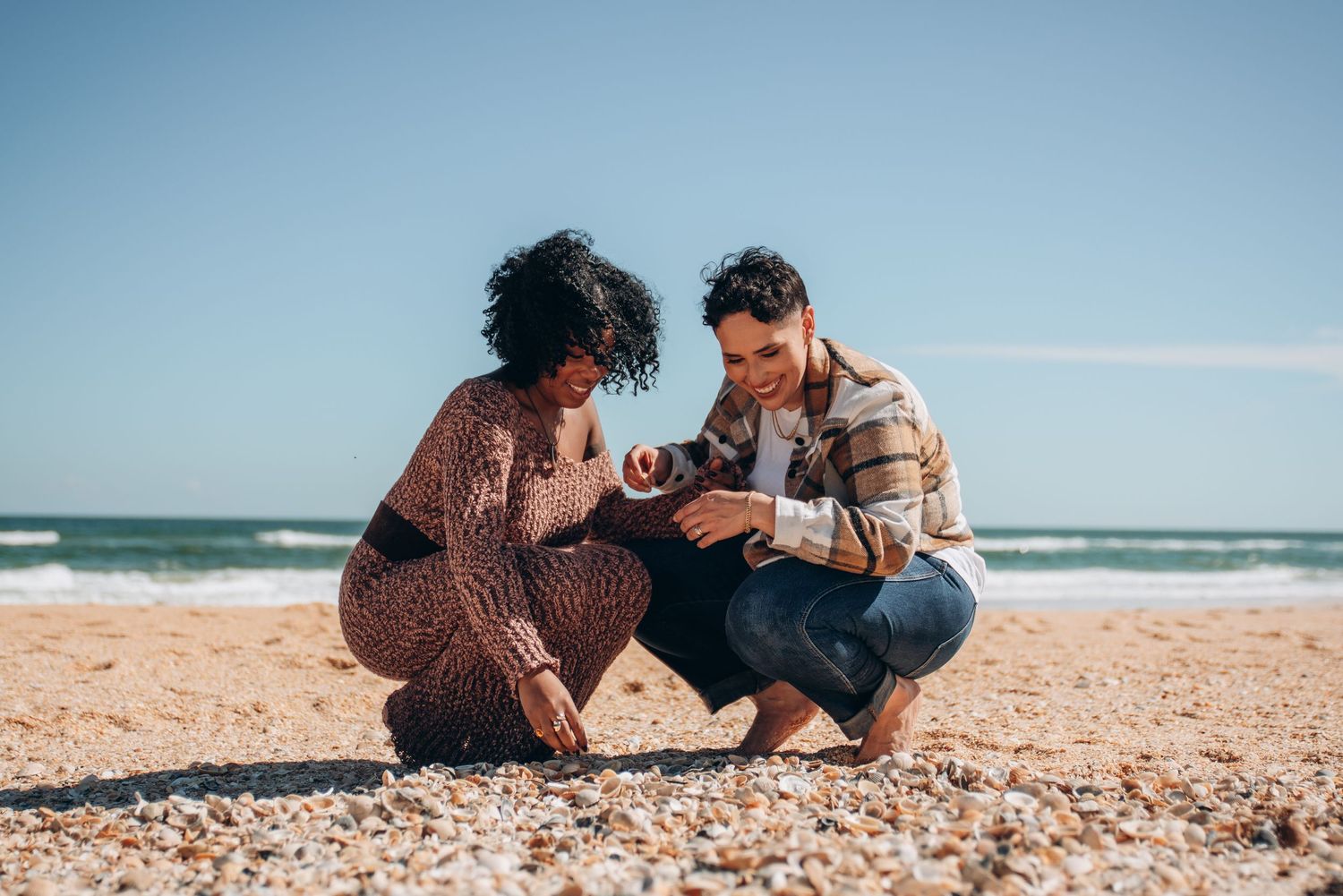 Two people sit close together on a sandy beach with ocean waves in the background.