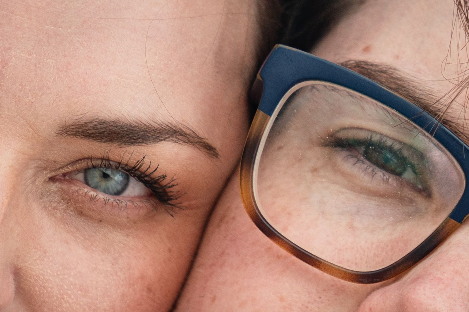Close up of two eyes side by side, one wearing blue gradient eyeglasses frames and one without glasses.
