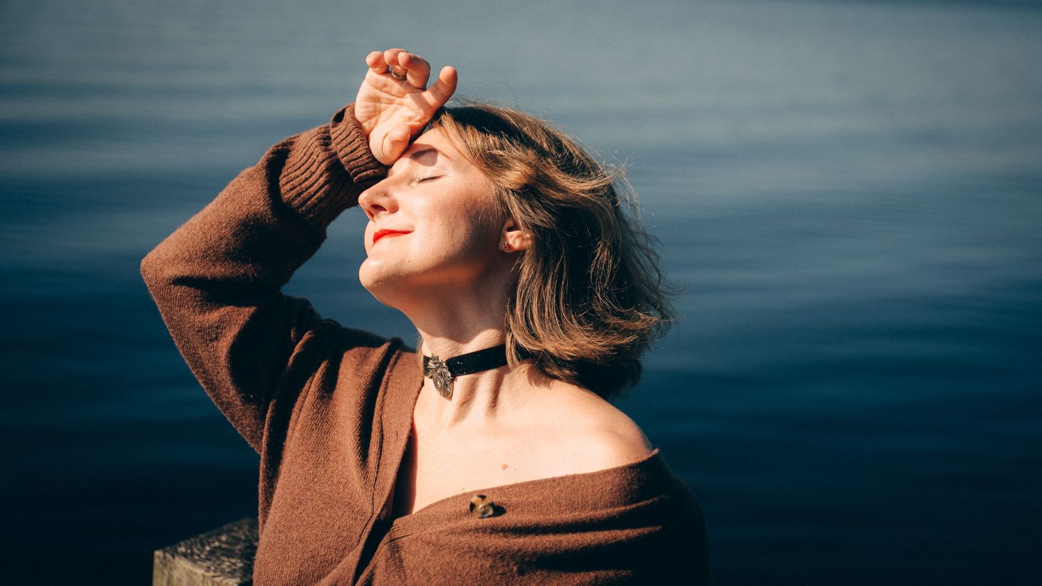 A woman in a brown coat poses against a moody blue sky in a series of artistic outdoor portraits.
