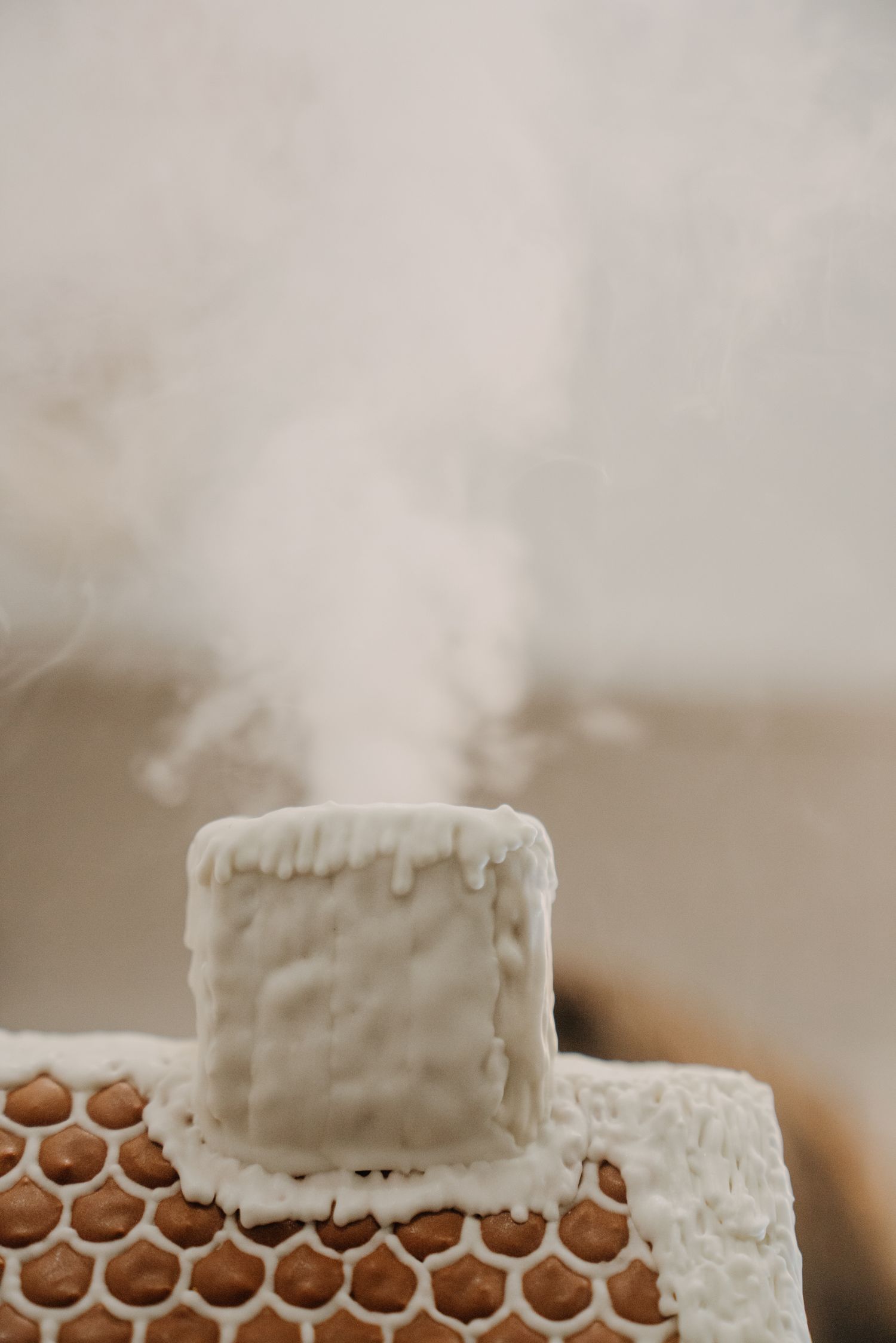 White frosted chimney on a gingerbread house emitting steam, decorated with icing drips on a honeycomb base.
