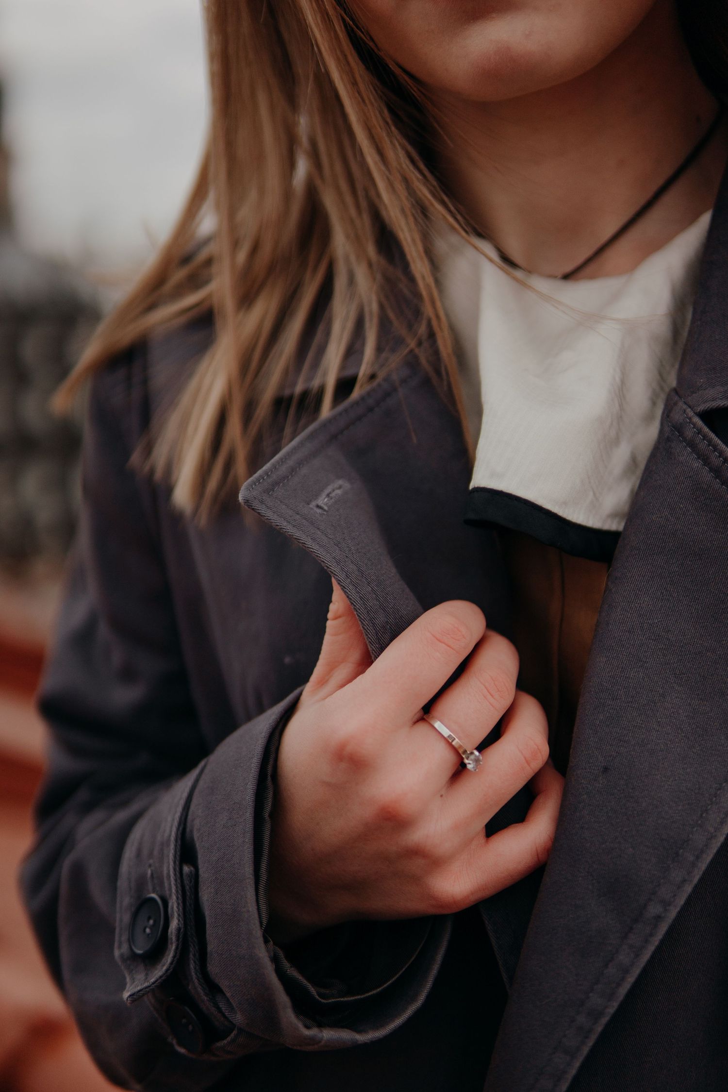 Woman in gray coat holding a small axe, wearing a delicate ring and black choker necklace.