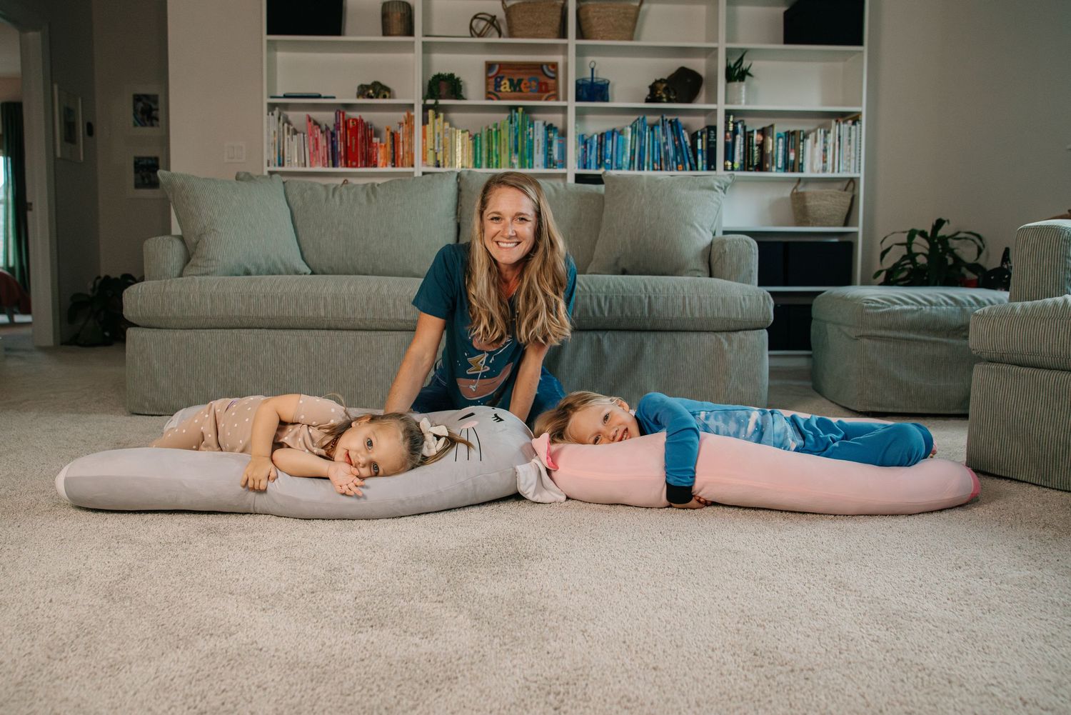 Woman smiling with two children lying on large floor pillows in cozy living room.