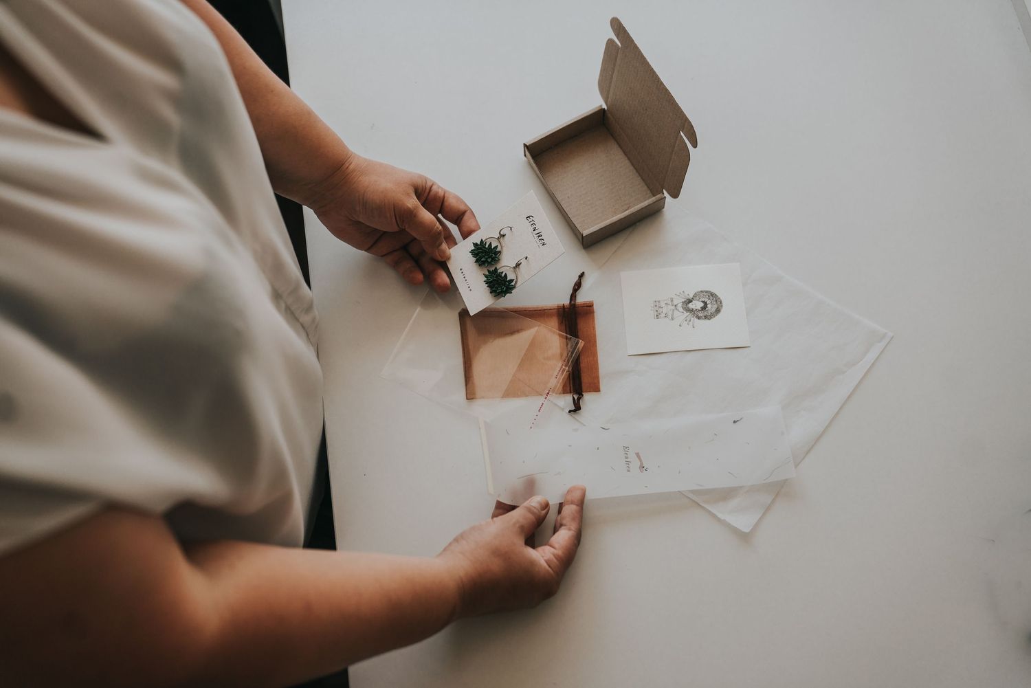 Person arranging elegant wedding stationery and invitation suite on a white table with kraft paper box.