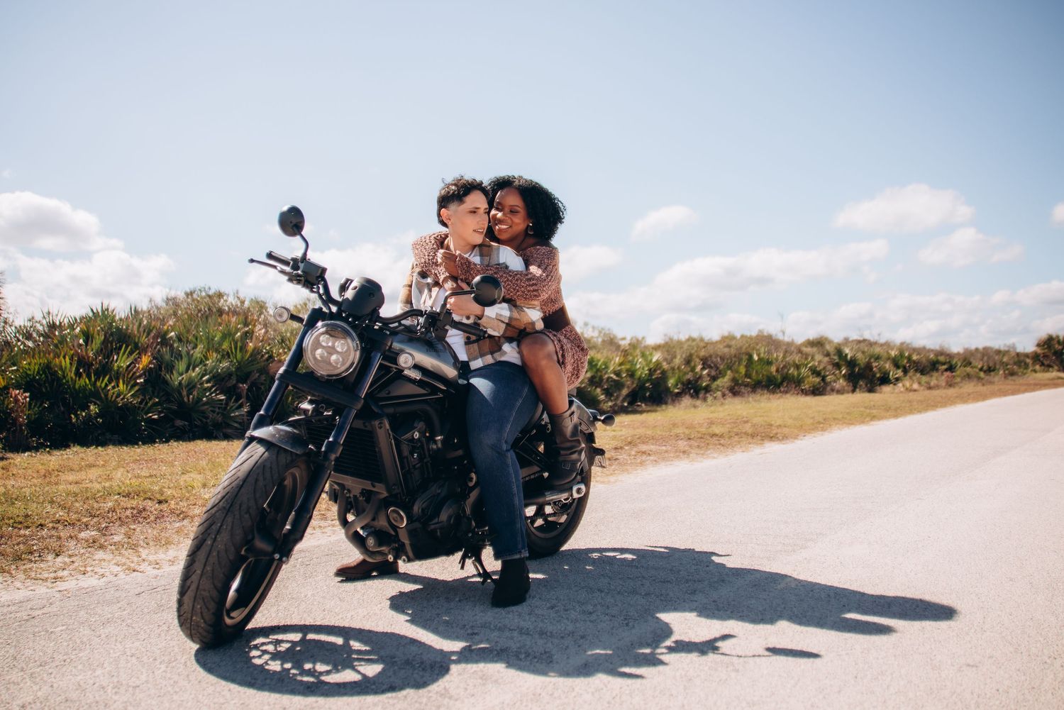 A black motorcycle parked on a sandy path against a bright blue sky.