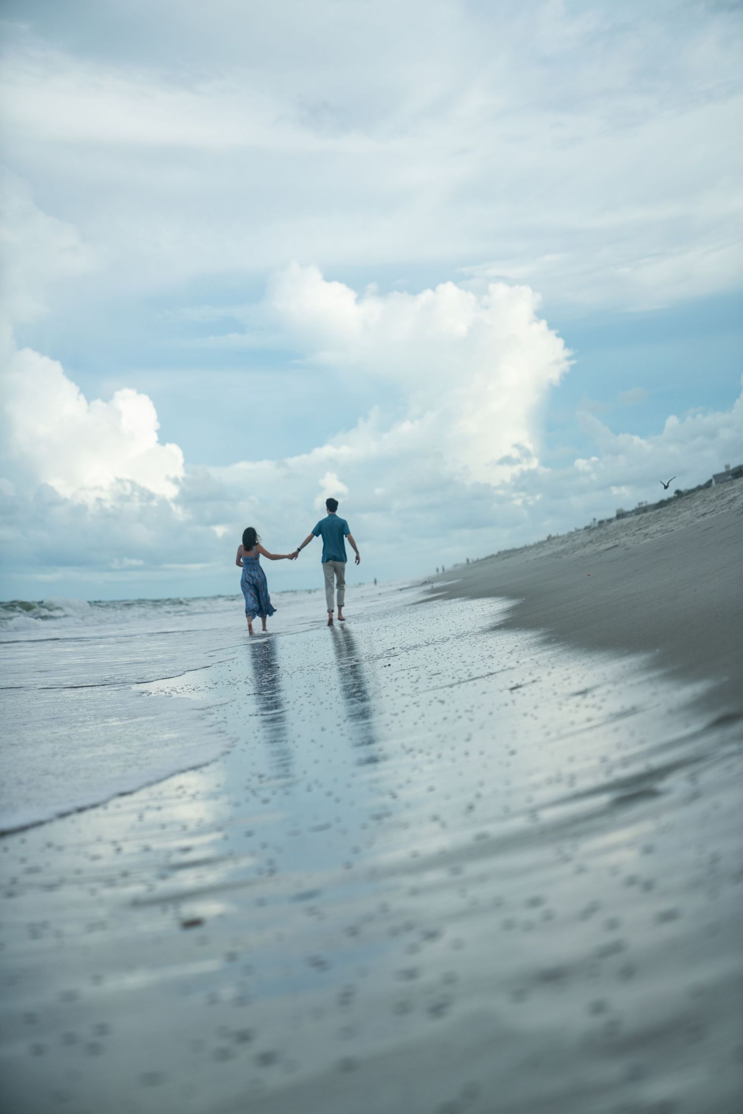 Two silhouetted figures walk together along a misty beach shoreline under cloudy skies.