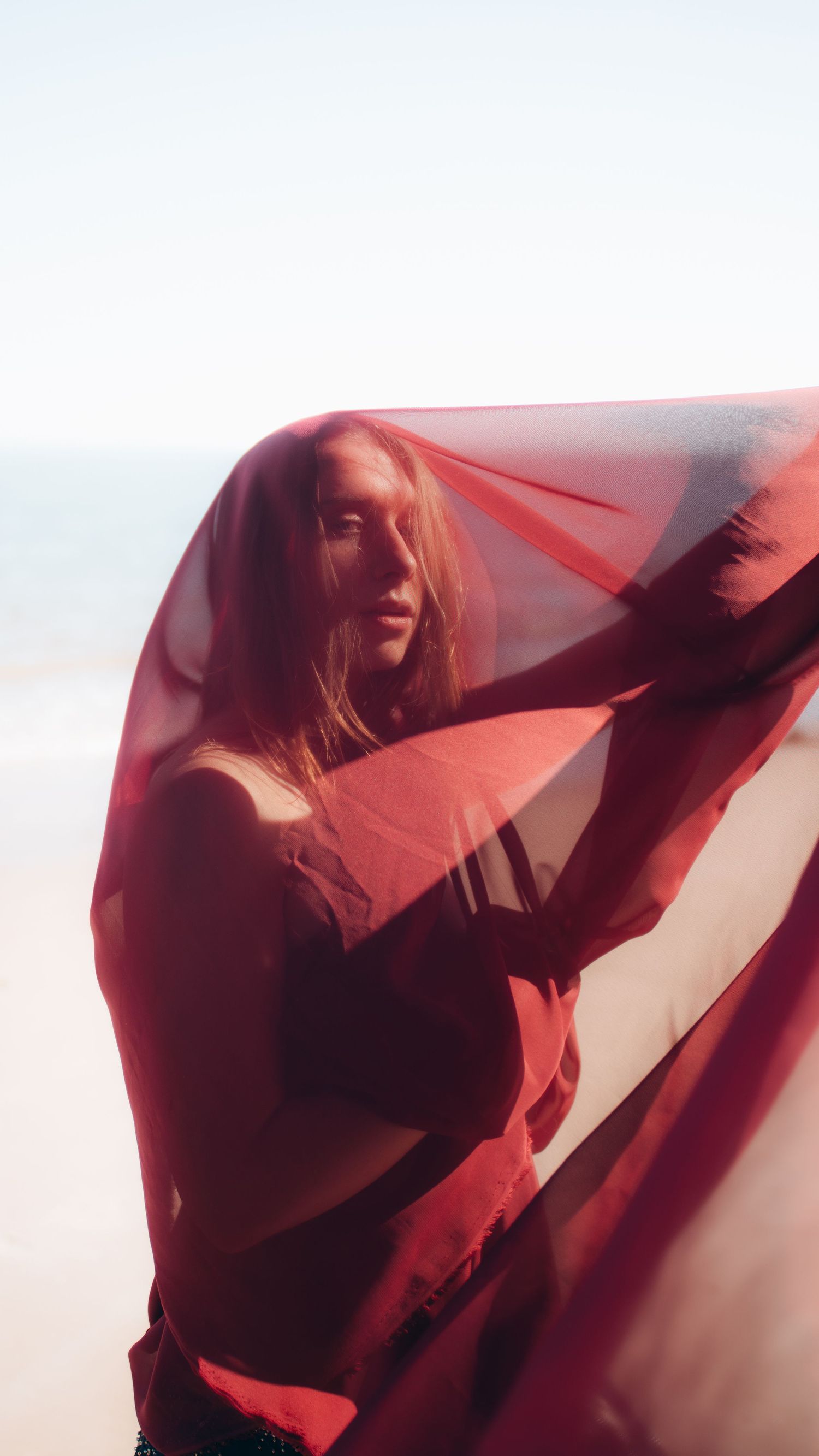 Ethereal silhouettes behind translucent red fabric create an artistic abstract composition.