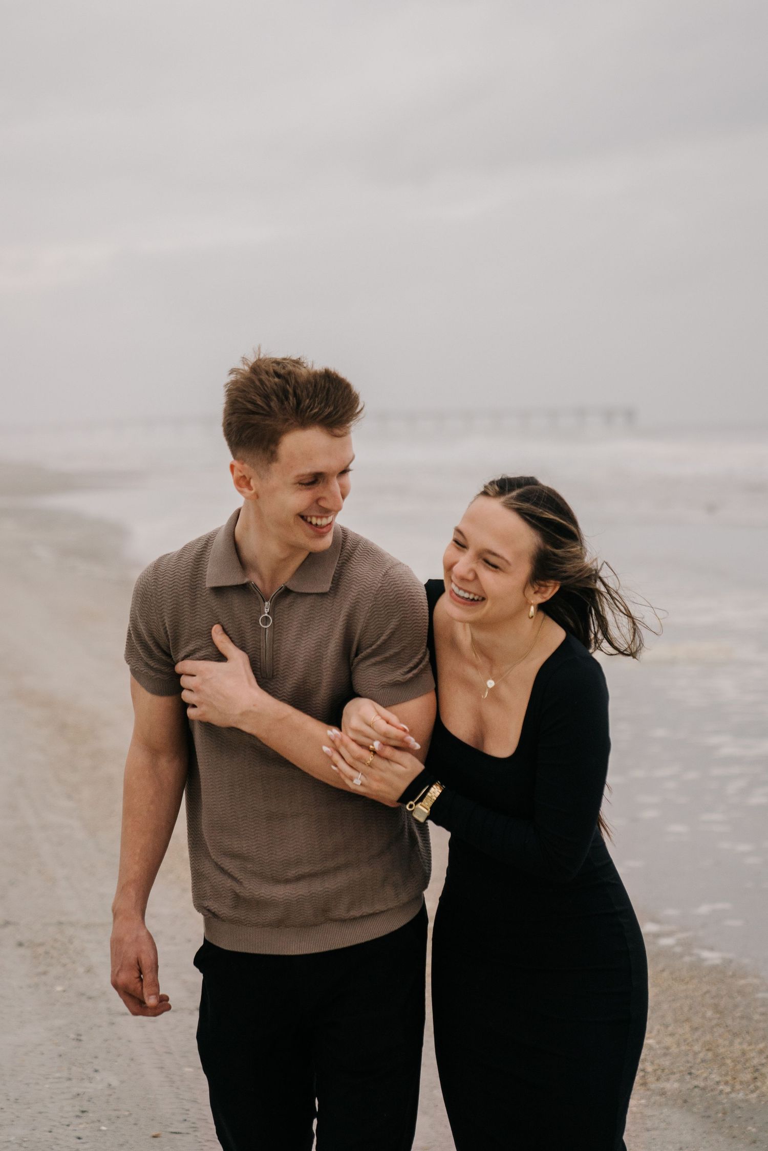 Two people share genuine laughter while walking together on a beach.