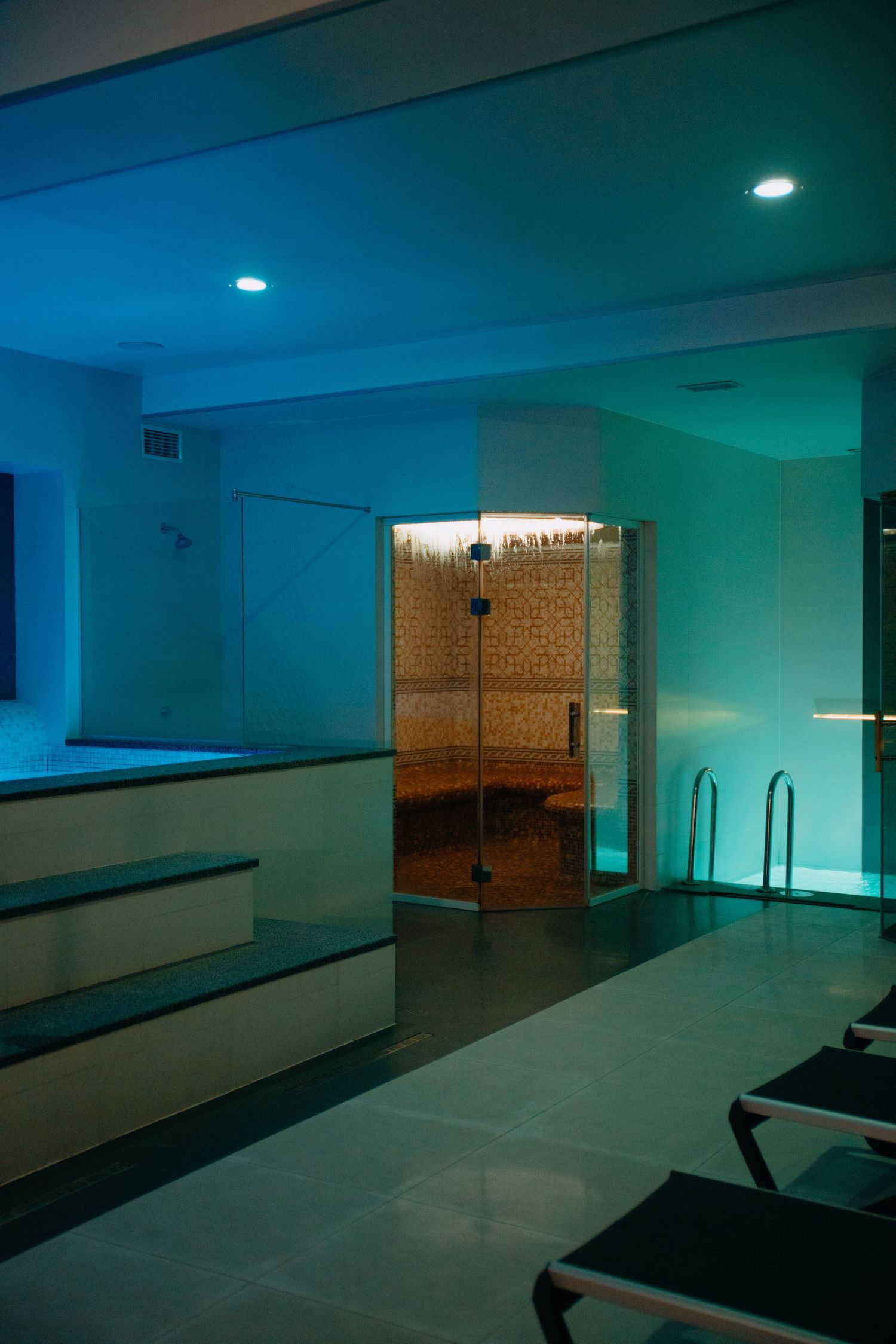 Modern spa relaxation area with teal ambient lighting and glass-enclosed sauna room.