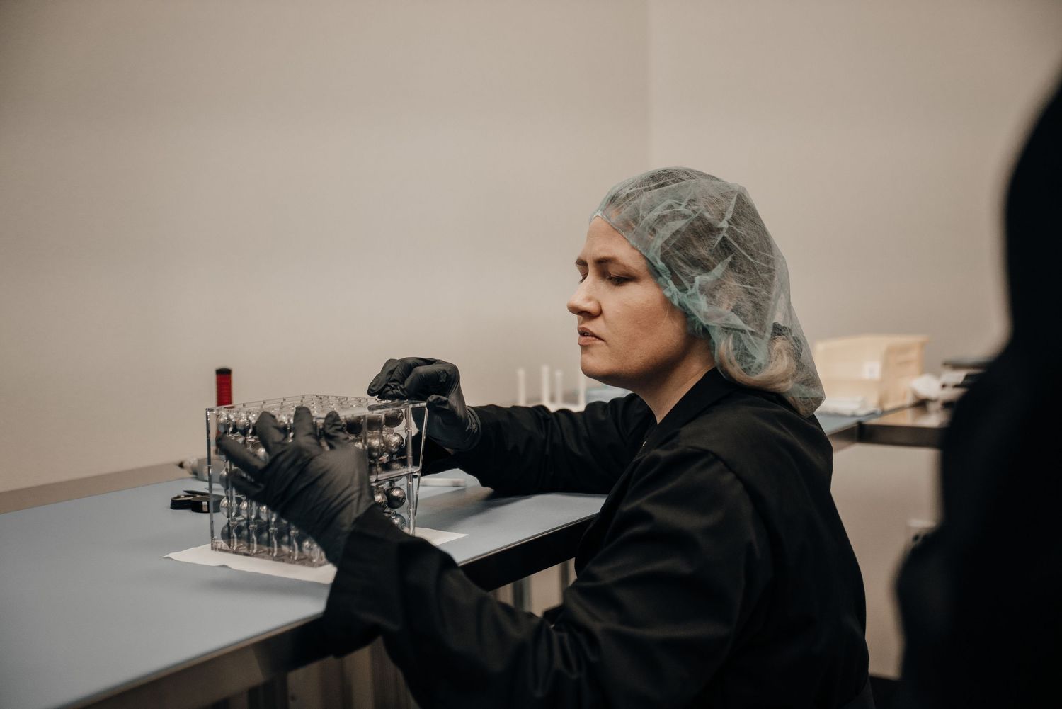 Female food industry worker in black uniform and hair net carefully handling laboratory equipment.