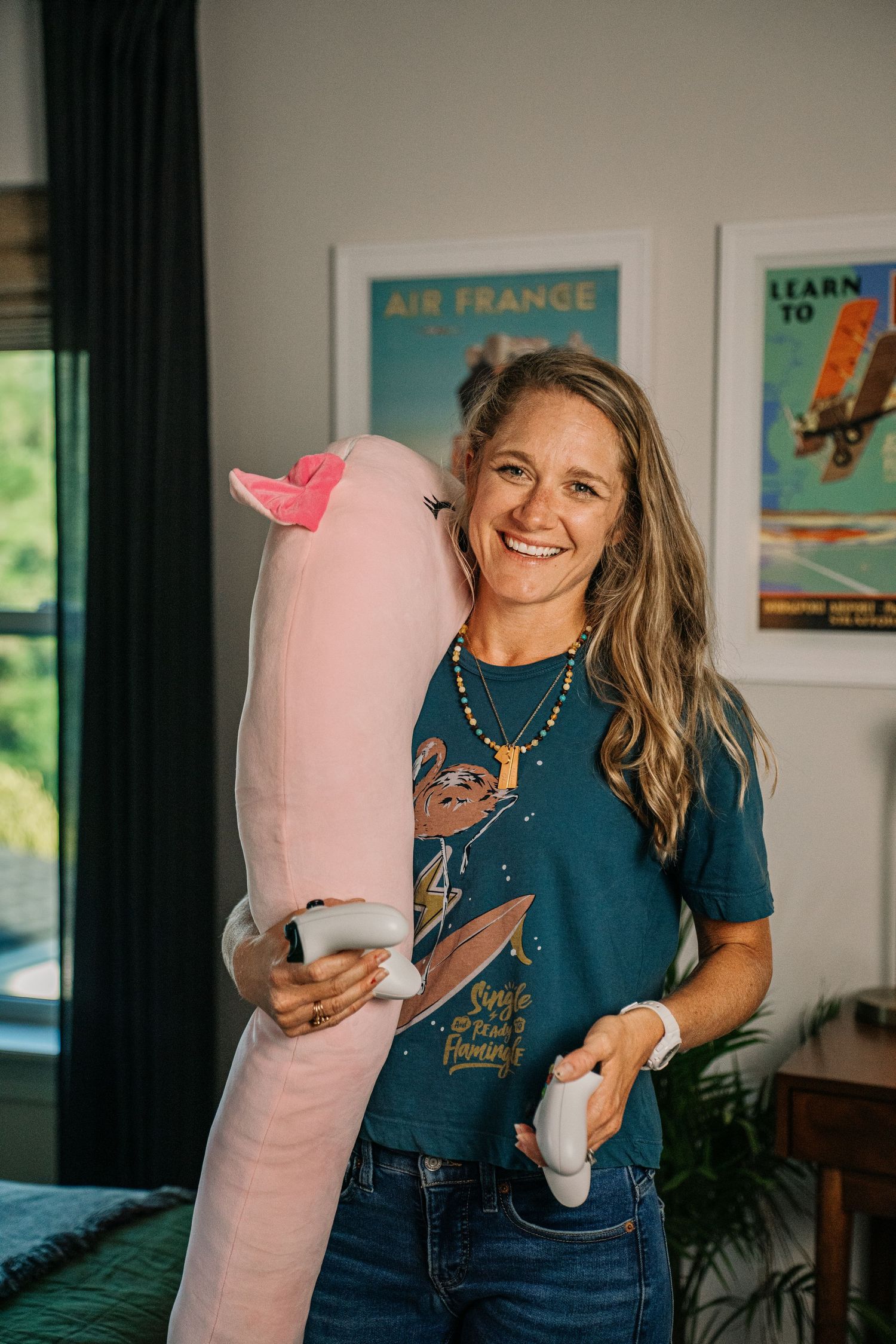 Smiling woman holding a large pink stuffed animal in a room with Air France and aviation posters.