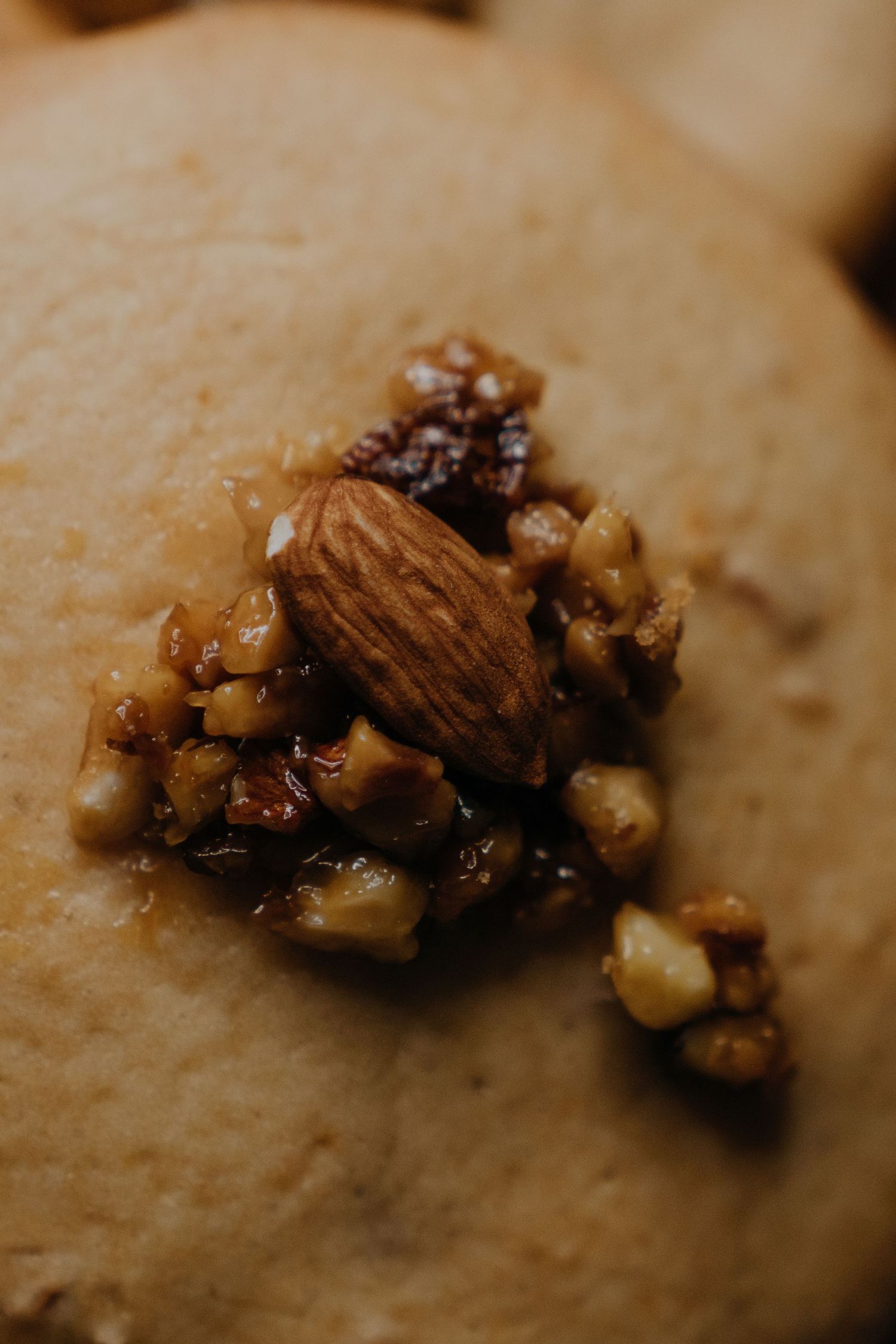 Close-up of a cookie topped with an almond and chopped walnuts in caramel glaze.