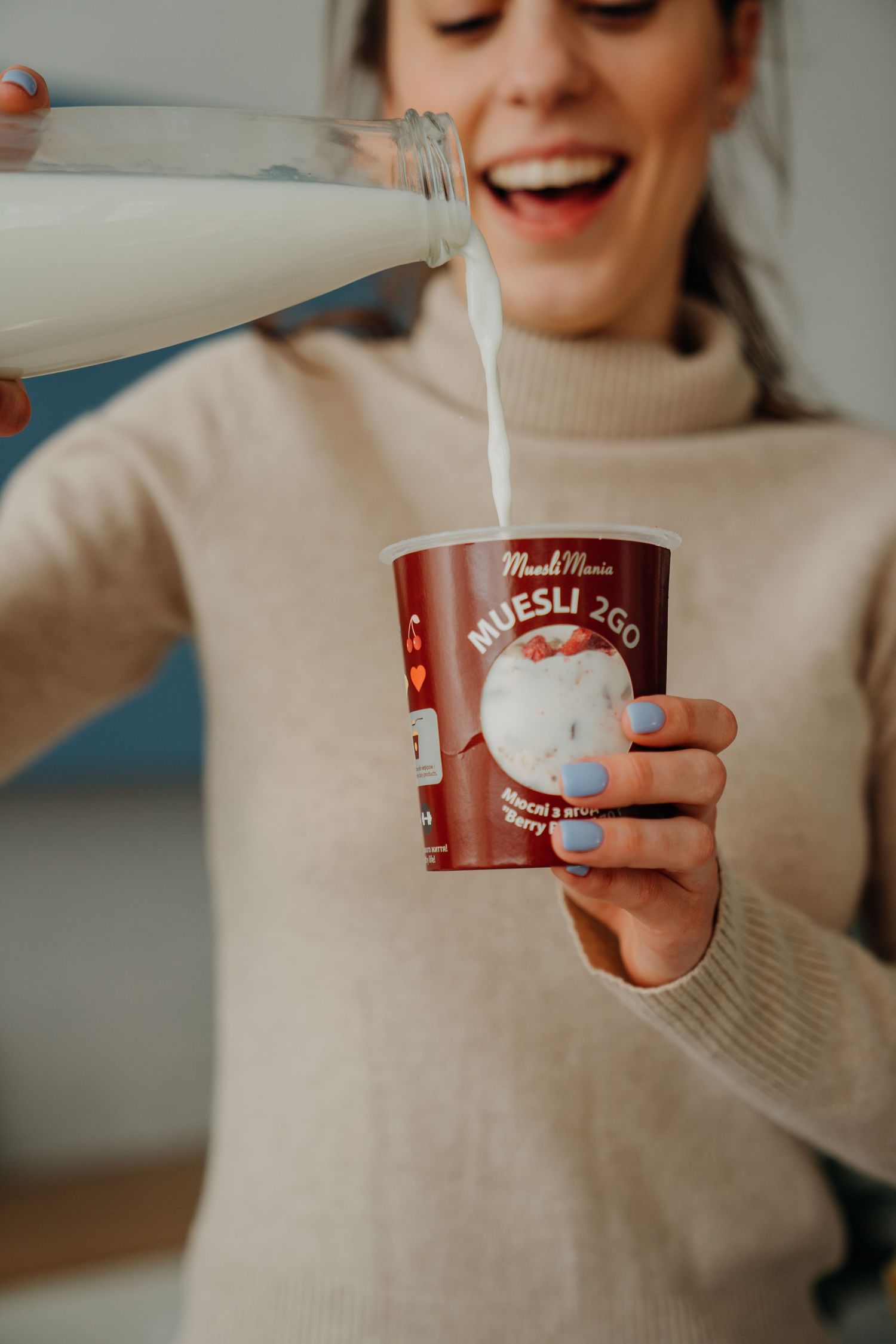 Woman pouring milk into a MuesliMania Muesli2Go cup while smiling.