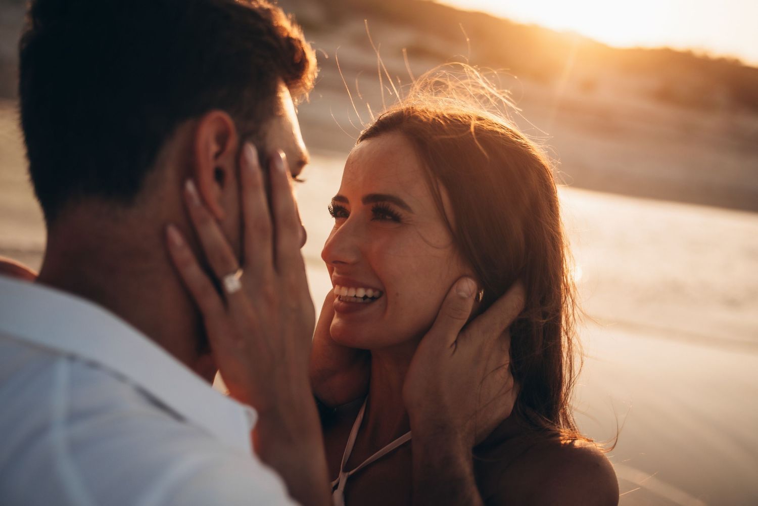 Romantic couple sharing a tender moment at sunset on the beach, woman smiling and touching man's face.